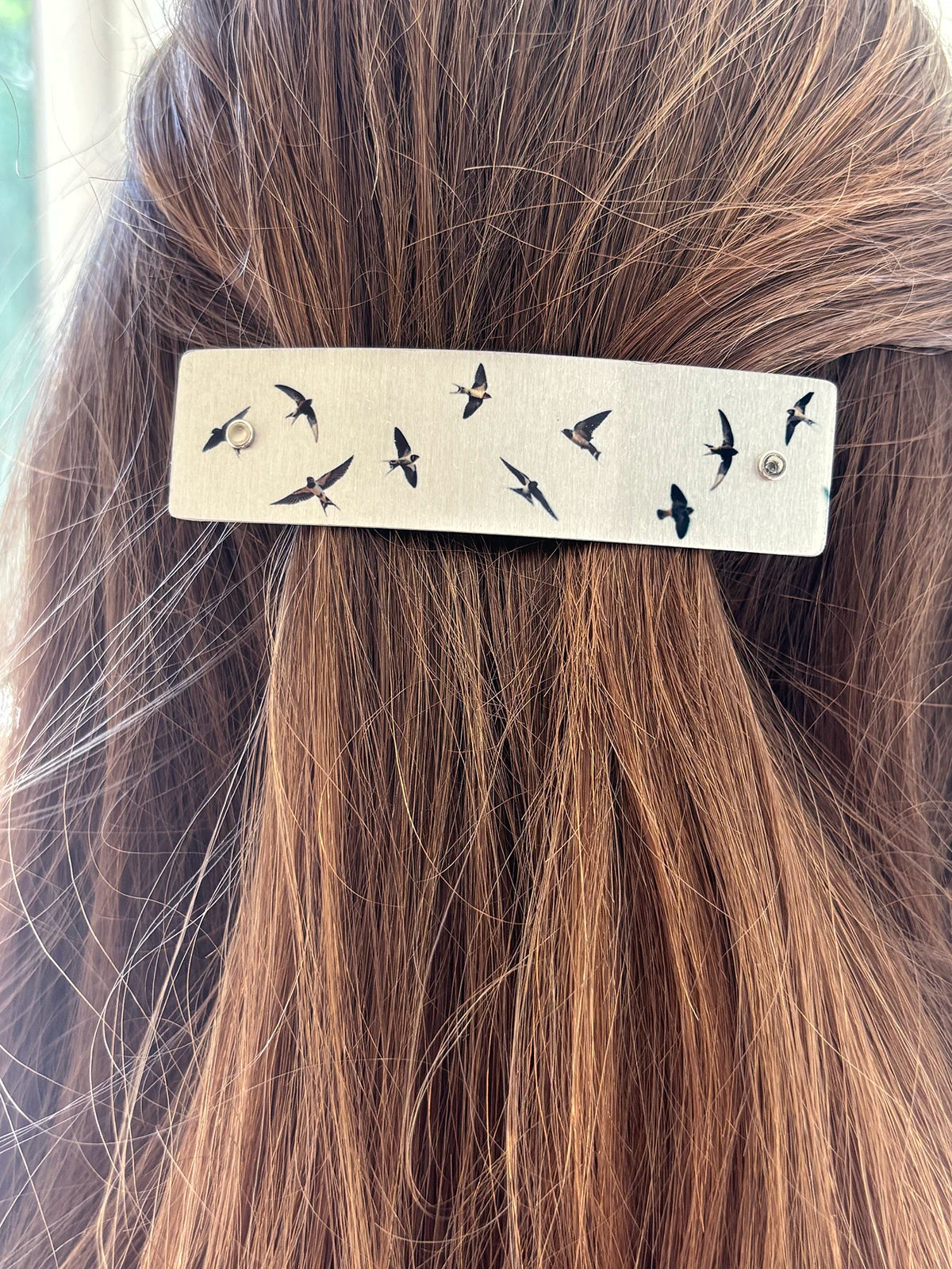 A close-up of a person's brown hair featuring a handmade metal hair clip adorned with small black flying bird silhouettes, by Robbin V. Davis Studio.