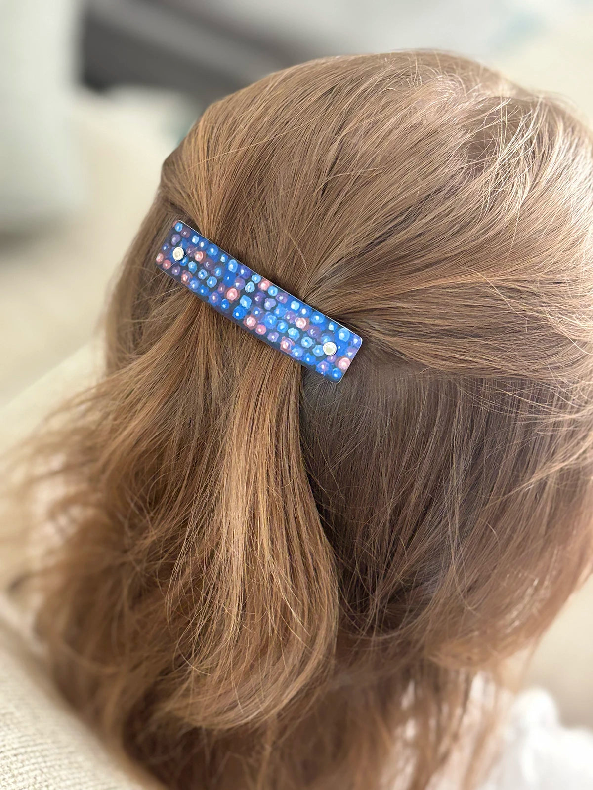A close-up of a child's light brown hair secured with a small rectangular hair clip decorated with an original blackberry pattern.