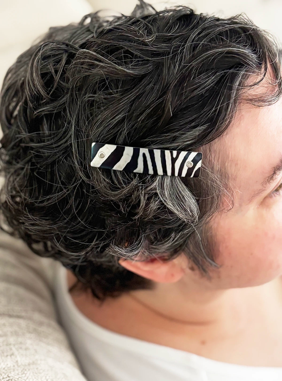 A close-up of a person's short, curly dark hair secured with a black and silver zebra-print hair clip.