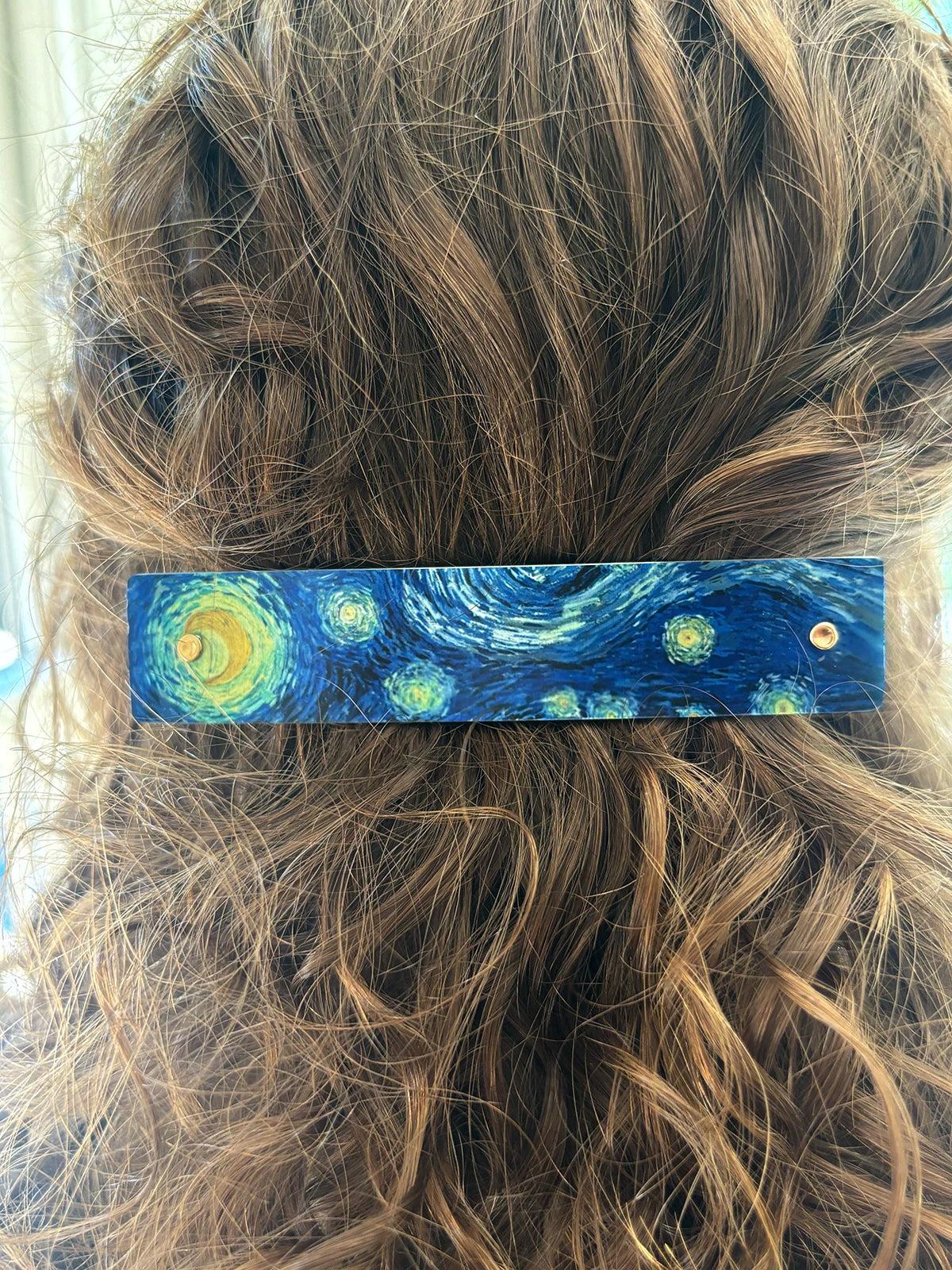 A close-up of a person's brown hair secured with a rectangular hair clip featuring a Van Gogh-inspired swirling blue and yellow night sky design.