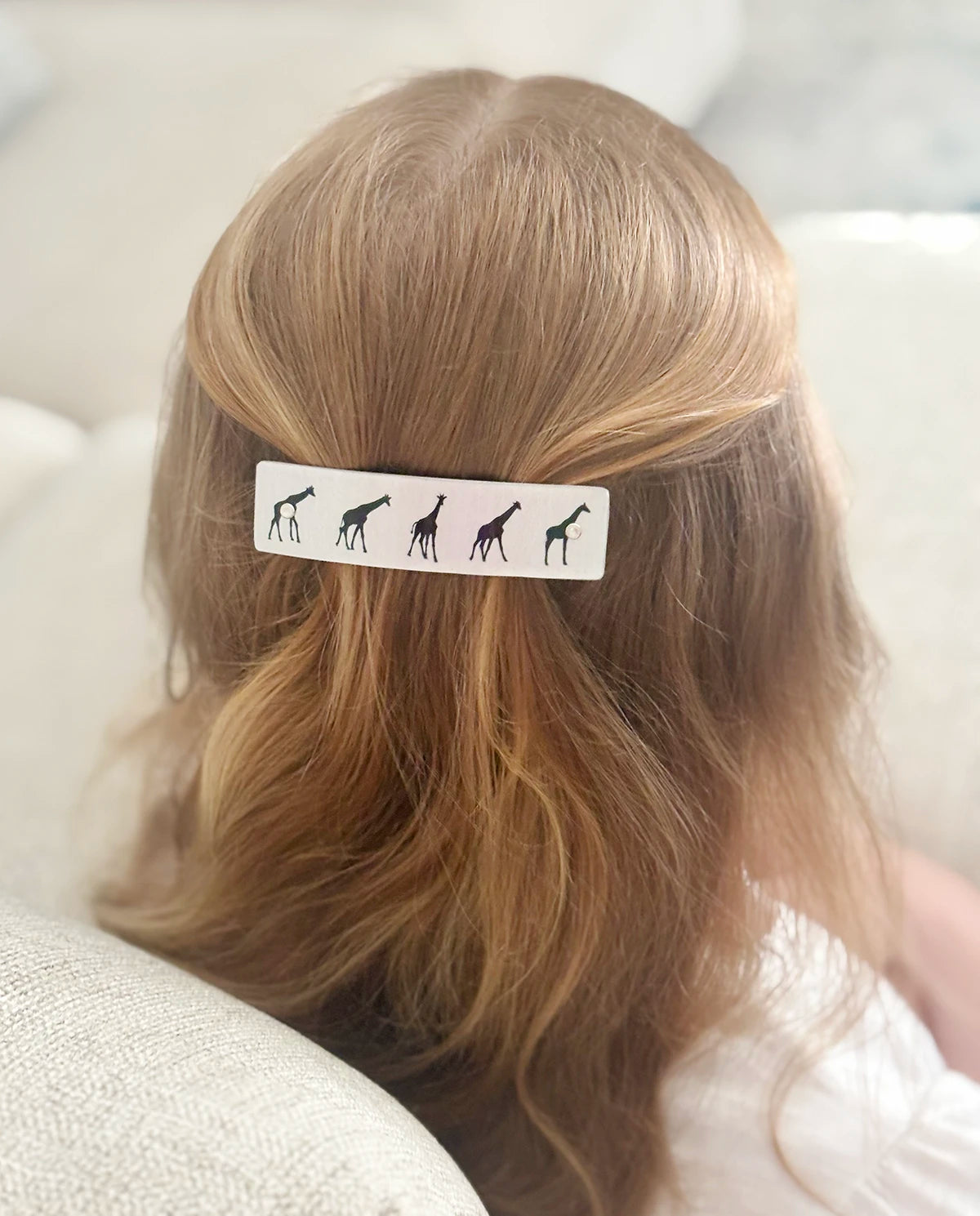 A close-up back view of a person with strawberry blond hair wearing a silver metal boutique hair clip decorated with black giraffe silhouettes.