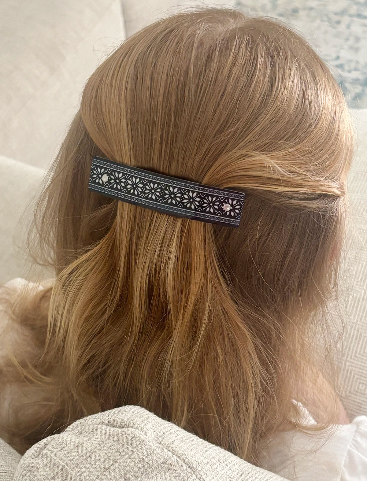 A close-up lifestyle shot of a woman's blonde hair secured with a black and silver star pattern French barrette, shown from behind.