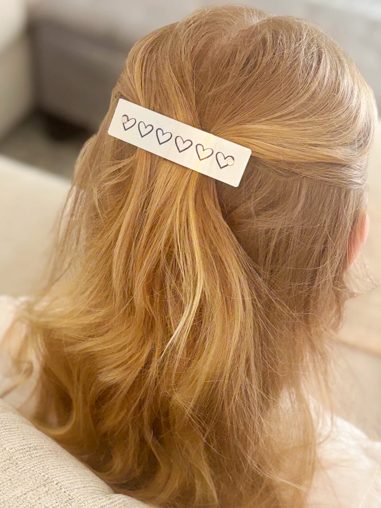 A close-up of a person's blonde hair secured with a silver rectangular hair clip decorated with five small outlined hearts.