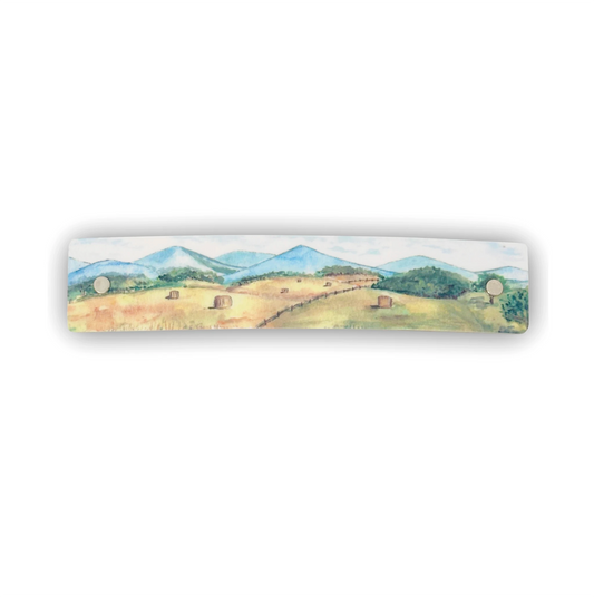 A rectangular boutique hair accessory featuring a watercolor landscape painting of a farm scene with hay rolls, trees, and mountains, shown against a plain white background.
