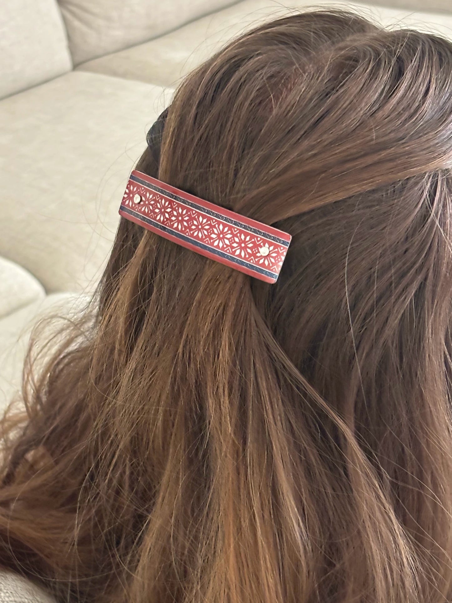 A close-up of a person's brown hair secured with a decorative hair clip. The clip features a red and black patterned band with silver snowflake-like motifs.