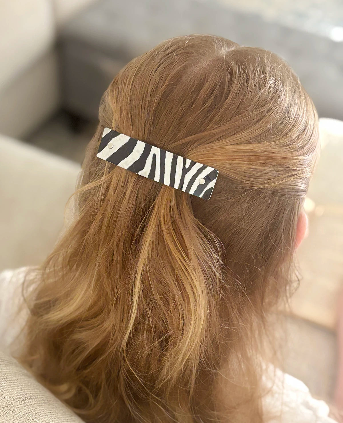 A close-up back view of a person with light brown hair wearing a black and white zebra-print hair clip.
