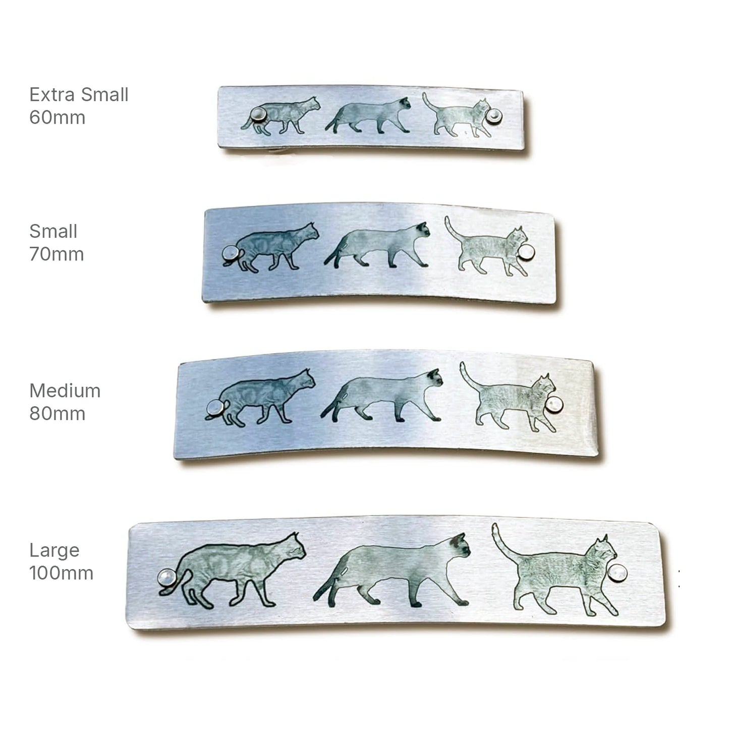 Four silver-toned metal hair clips with original cat illustrations, shown in four sizes labeled Extra Small 60mm, Small 70mm, Medium 80mm, and Large 100mm on a white background.