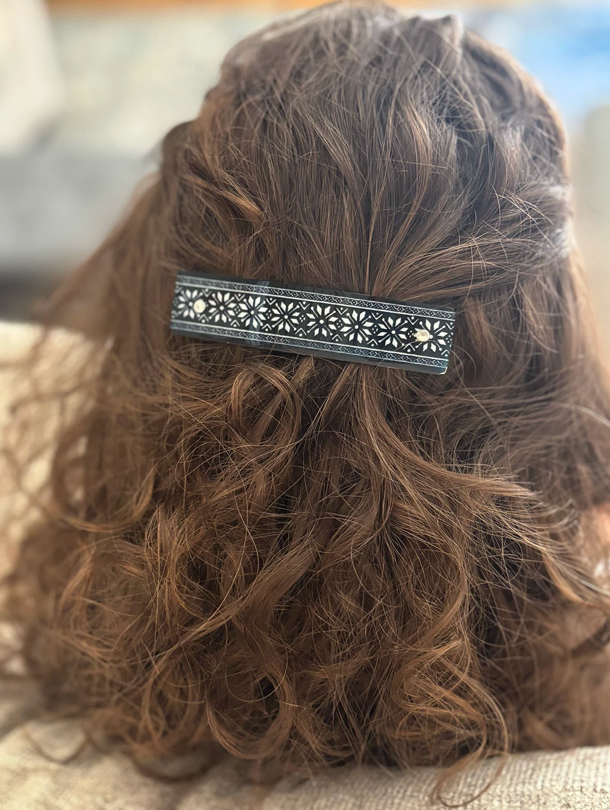 A close-up back view of a person with brown curly hair wearing a decorative black and silver-toned metal hair clip with a floral or star cutout pattern.