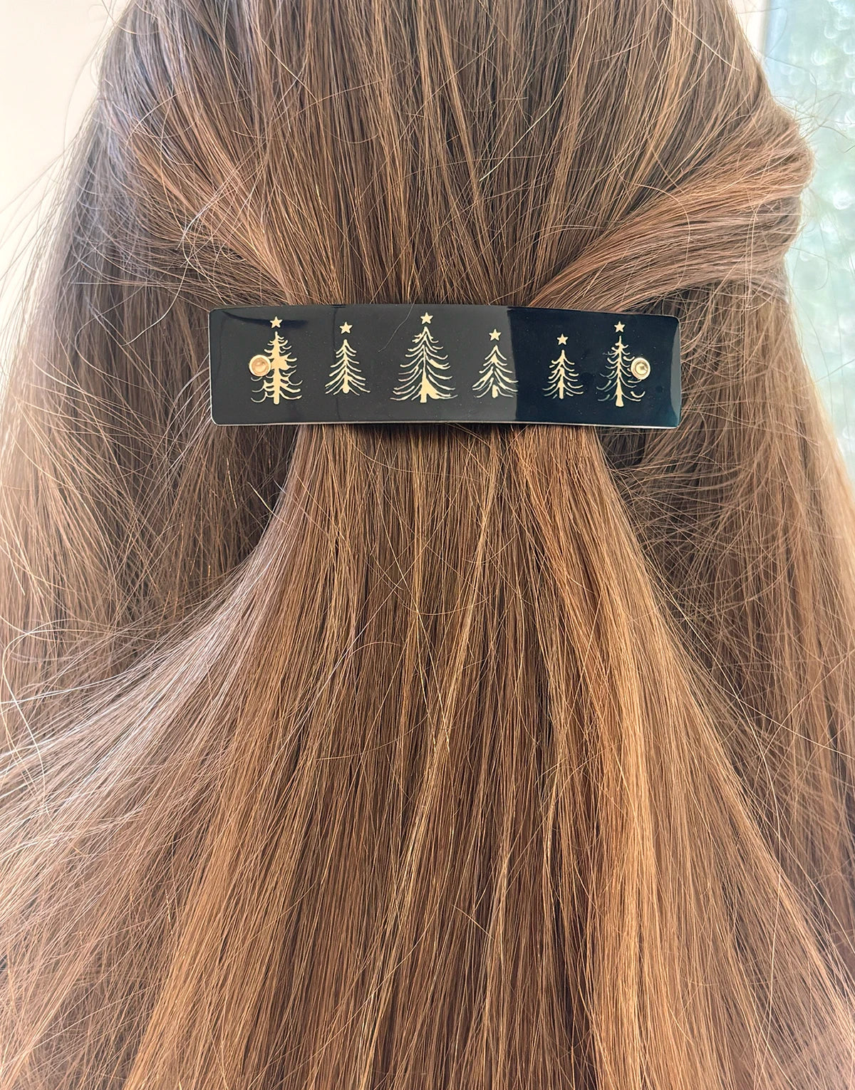 A close-up of a person's light brown hair secured with a black hair clip decorated with gold tree and star motifs.