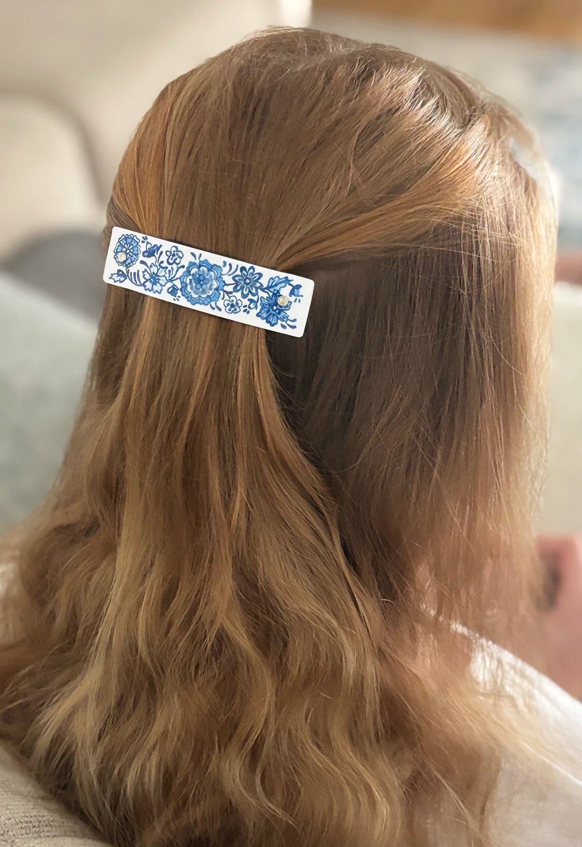 A close-up lifestyle shot of a person's blonde hair secured with a white hair clip decorated with a blue floral pattern.