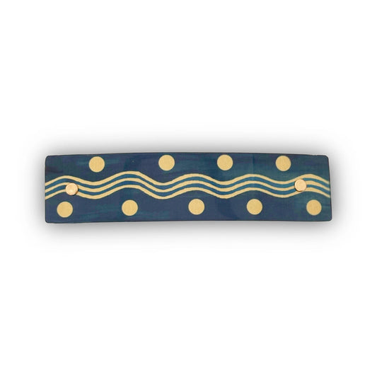 A rectangular hair barrette with a gold wavy line and polka dot pattern, shown against a plain white background.