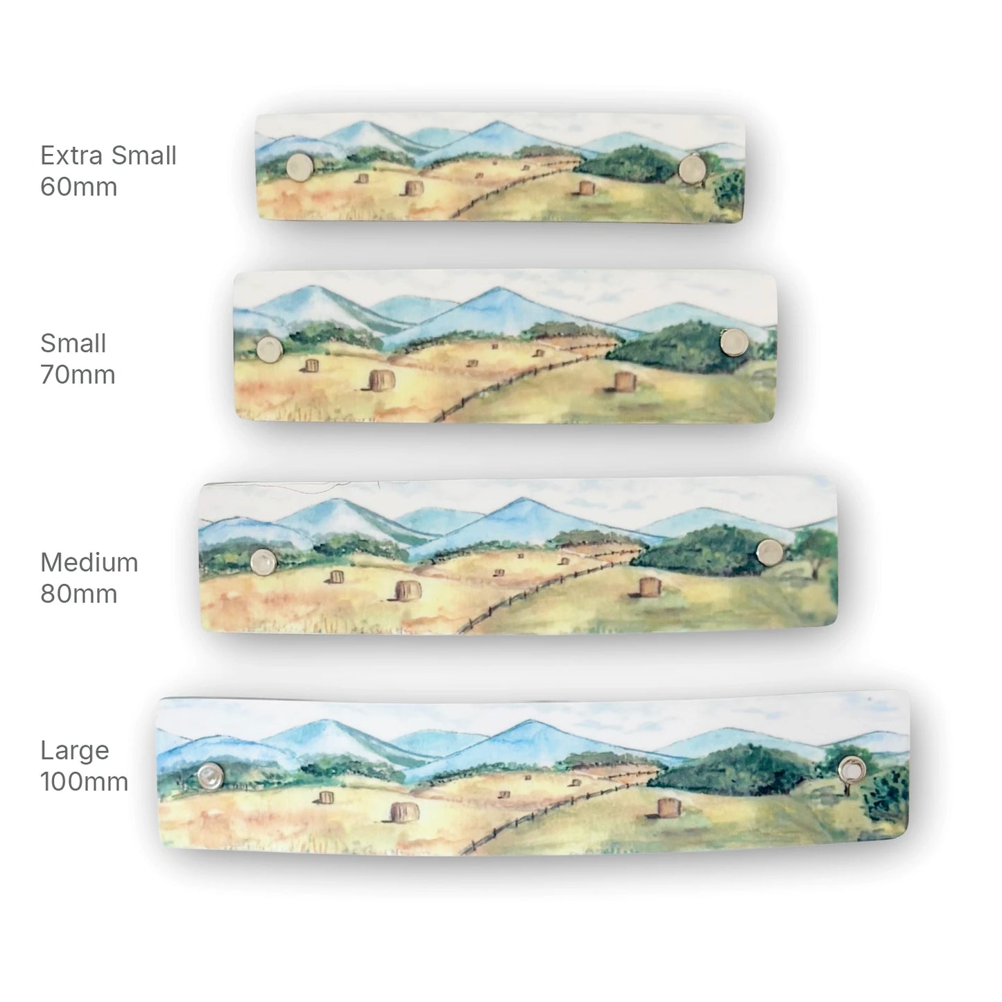Four rectan boutique hair clips shown in different sizes (Extra Small 60mm, Small 70mm, Medium 80mm, Large 100mm) lined up vertically on a white background. Each barrette features a watercolor landscape of a green valley with hayriolls and blue mountains.