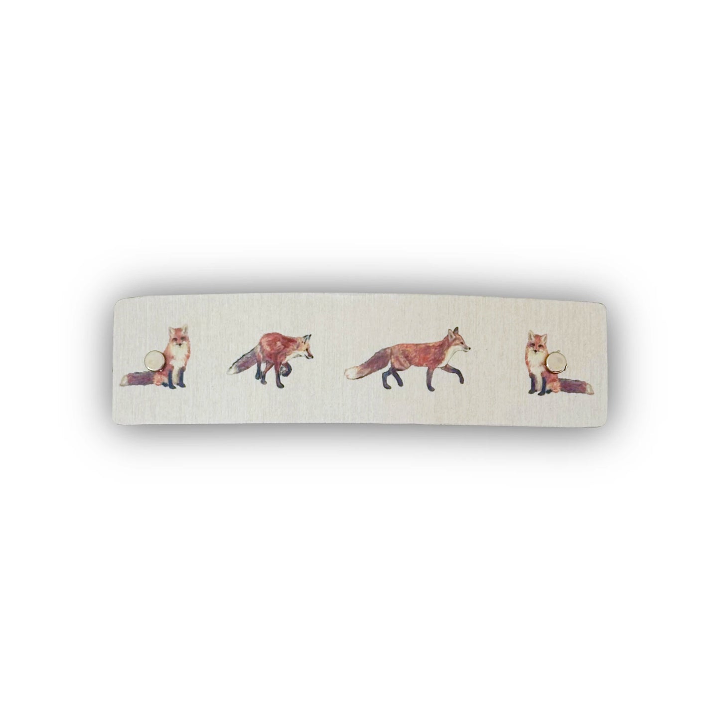 A rectangular hair barrette with rounded corners, featuring a silver metallic background printed with a row of watercolor-style foxes in shades of orange, brown, and cream.