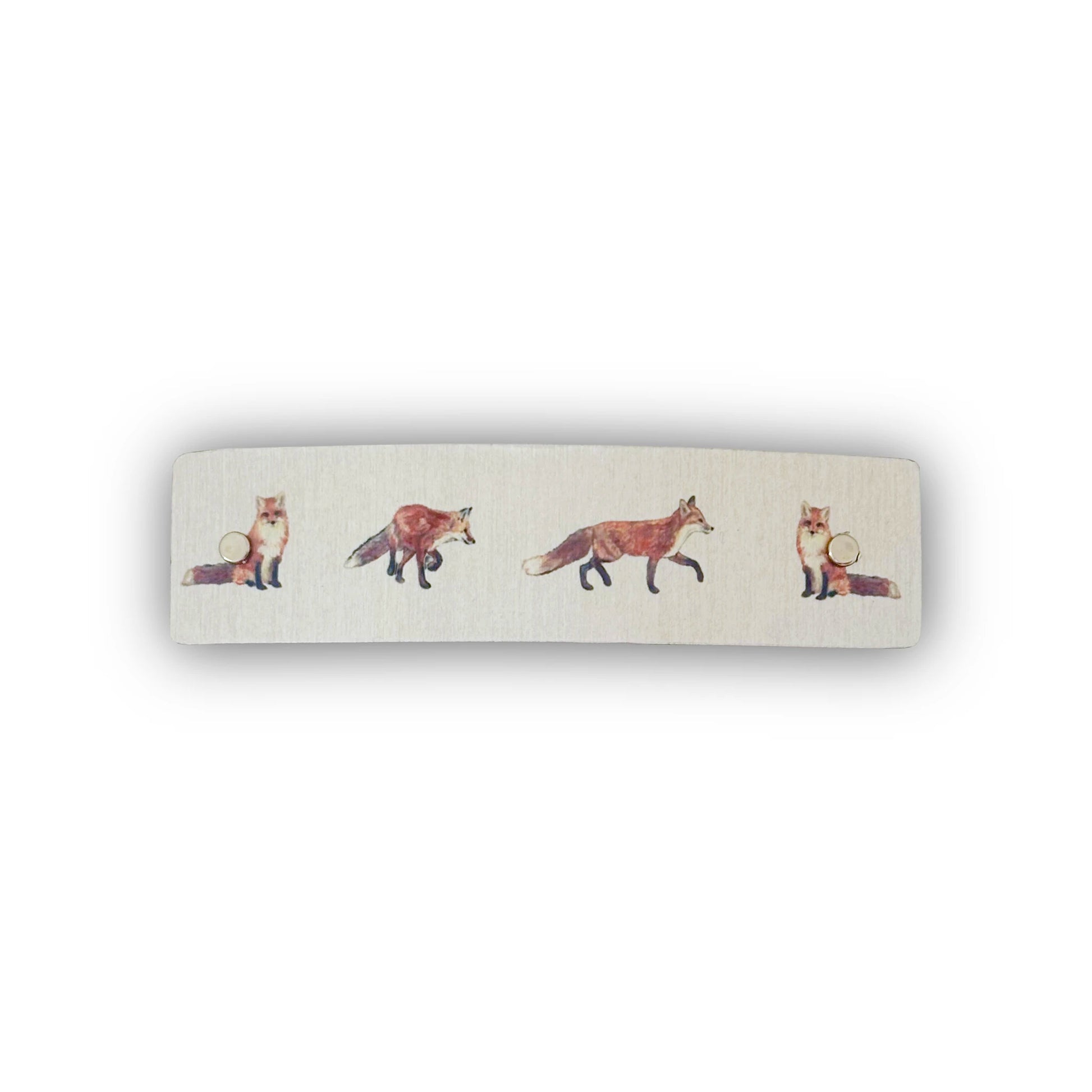 A rectangular hair barrette with rounded corners, featuring a silver metallic background printed with a row of watercolor-style foxes in shades of orange, brown, and cream.