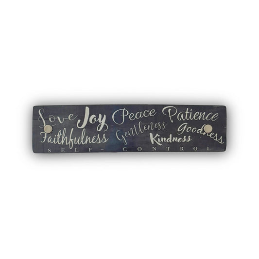 A rectangular dark gray French barrette with silver hand-lettered text listing virtues such as love, joy, peace, patience, kindness, and goodness, shown on a plain white background.
