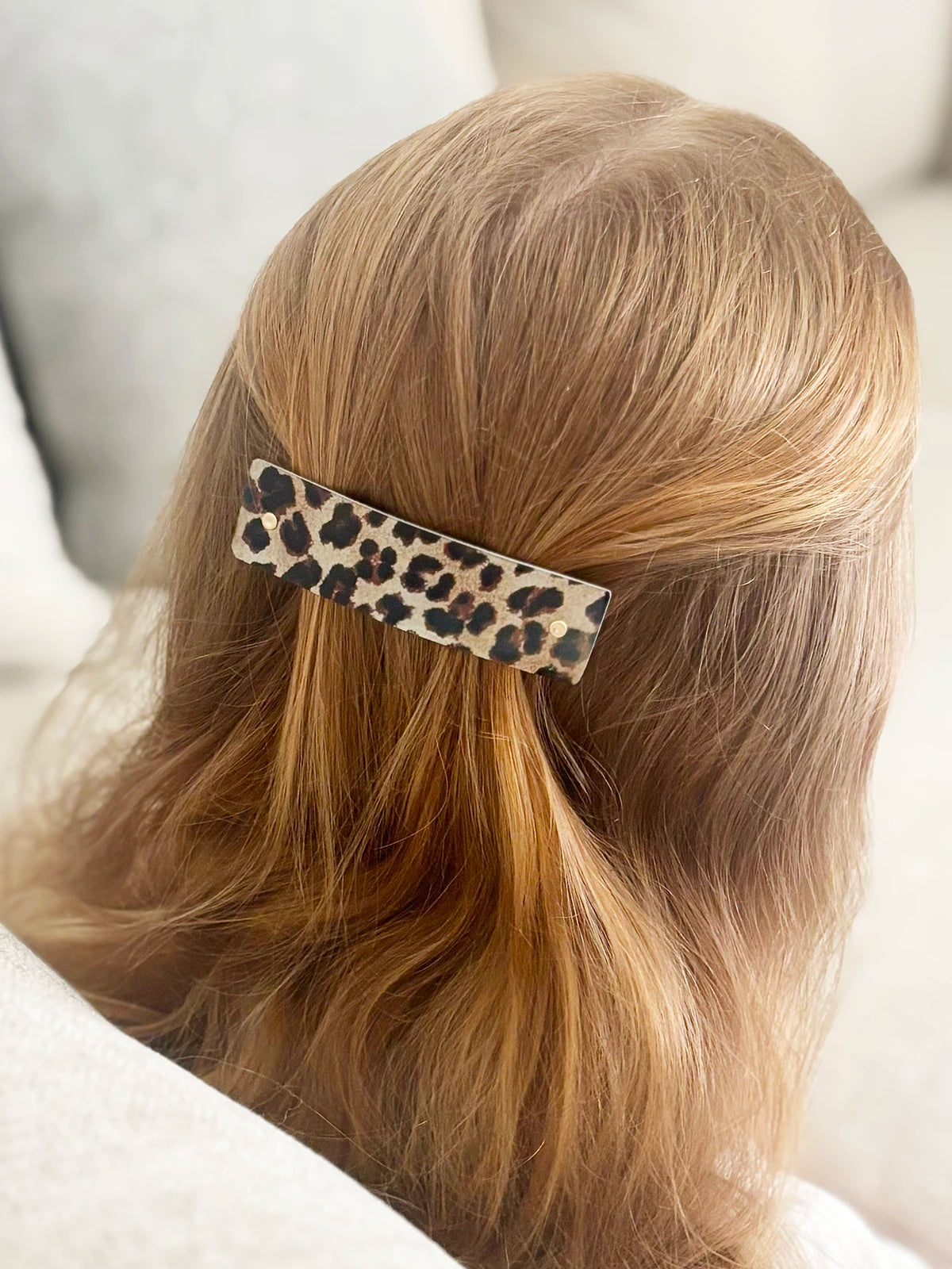A close-up lifestyle shot of a person's blonde hair secured with a leopard print hair clip, viewed from behind.