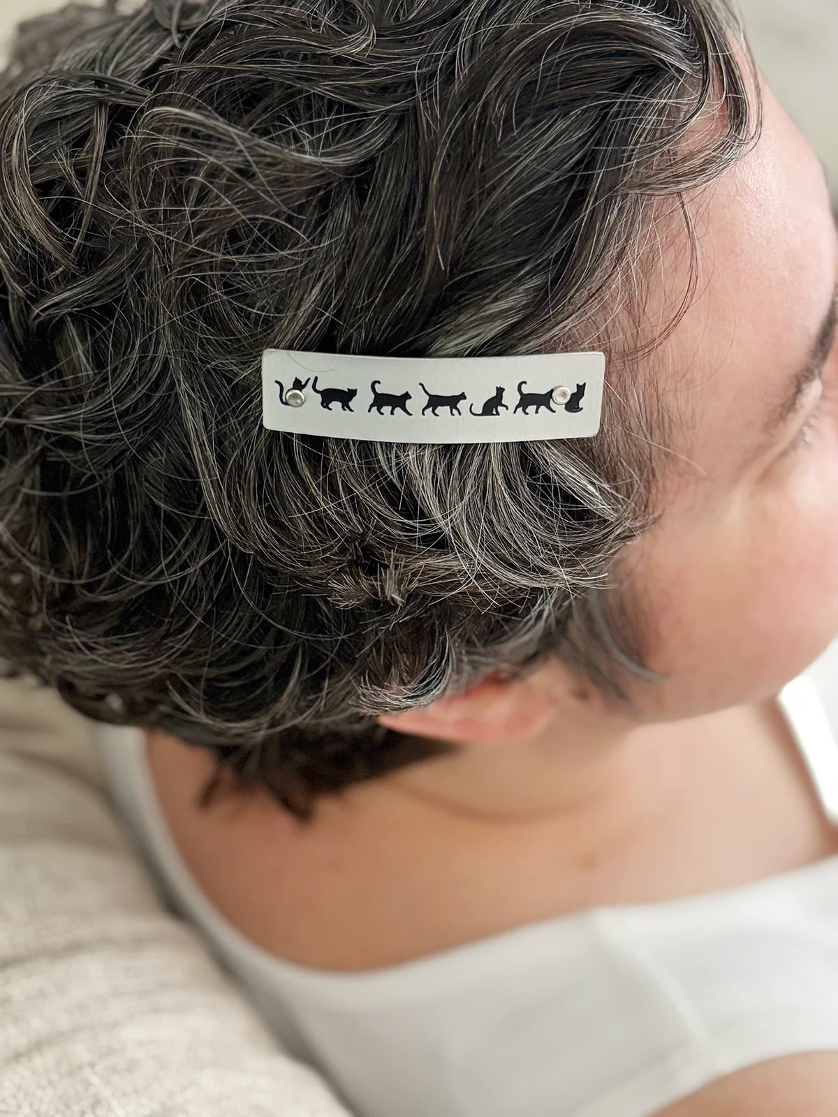 A close-up of a person's short, curly gray hair wearing a silver hair clip decorated with black cat silhouettes.