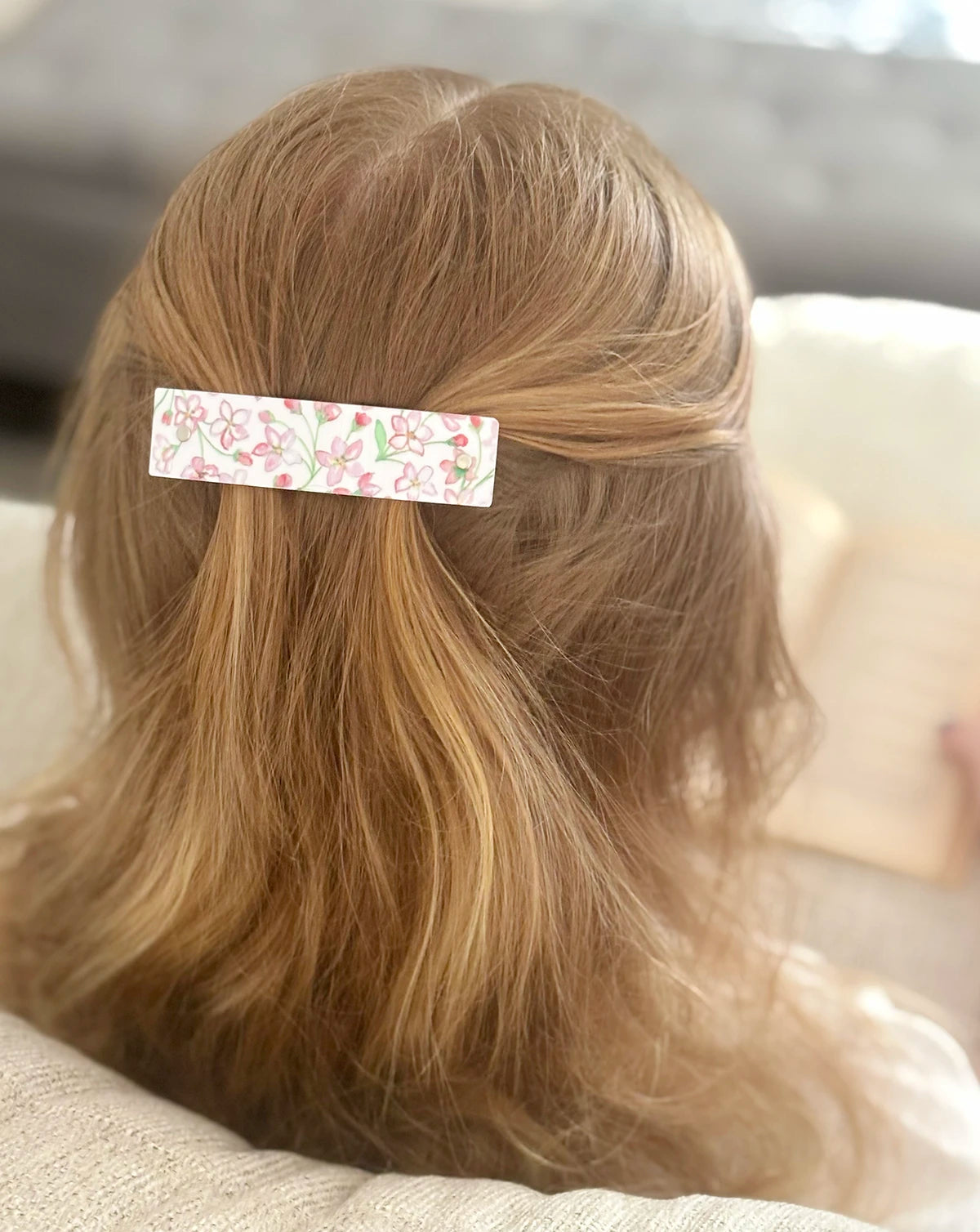 A close-up back view of a person with strawberry blond hair,  wearing a rectangular hair clip decorated with watercolor pink and green floral artwork on a white background.