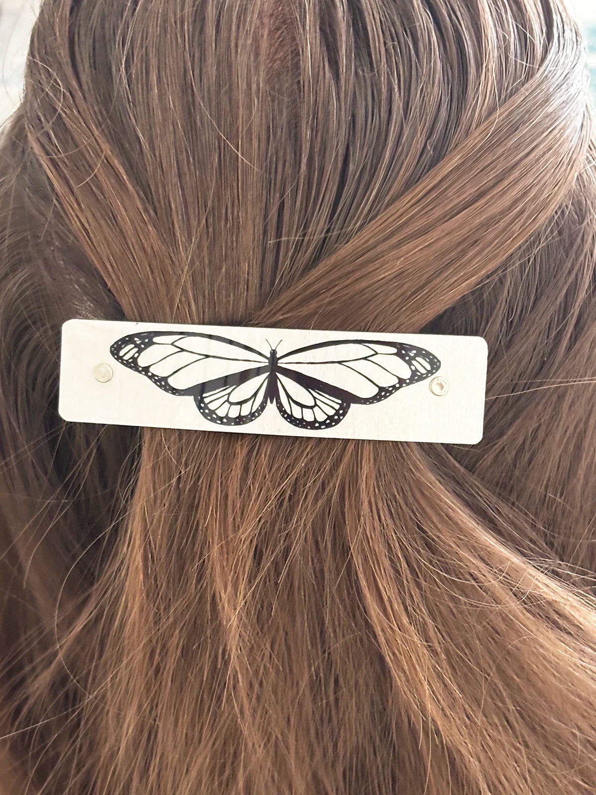 French barrette featuring a butterfly outline in black on silver, clipped into brown hair.