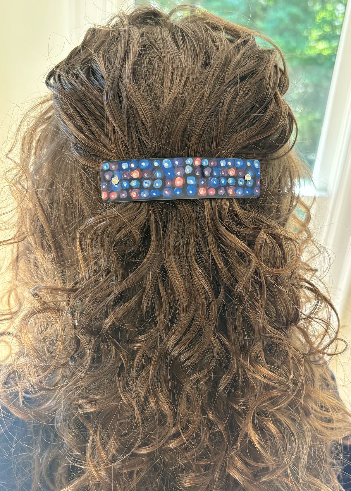 A close-up back view of a person with long, wavy brown hair wearing a rectangular hair clip adorned with original blackberry inspired design.