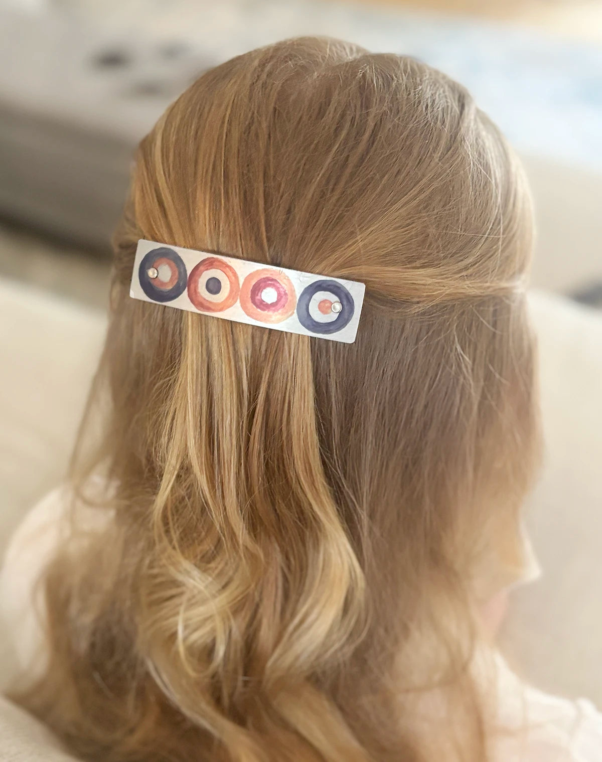 Handmade metal barrette with a design of soft earthy circles in neutral, natural colors, by Robbin V. Davis Studio, shown on long blond hair.