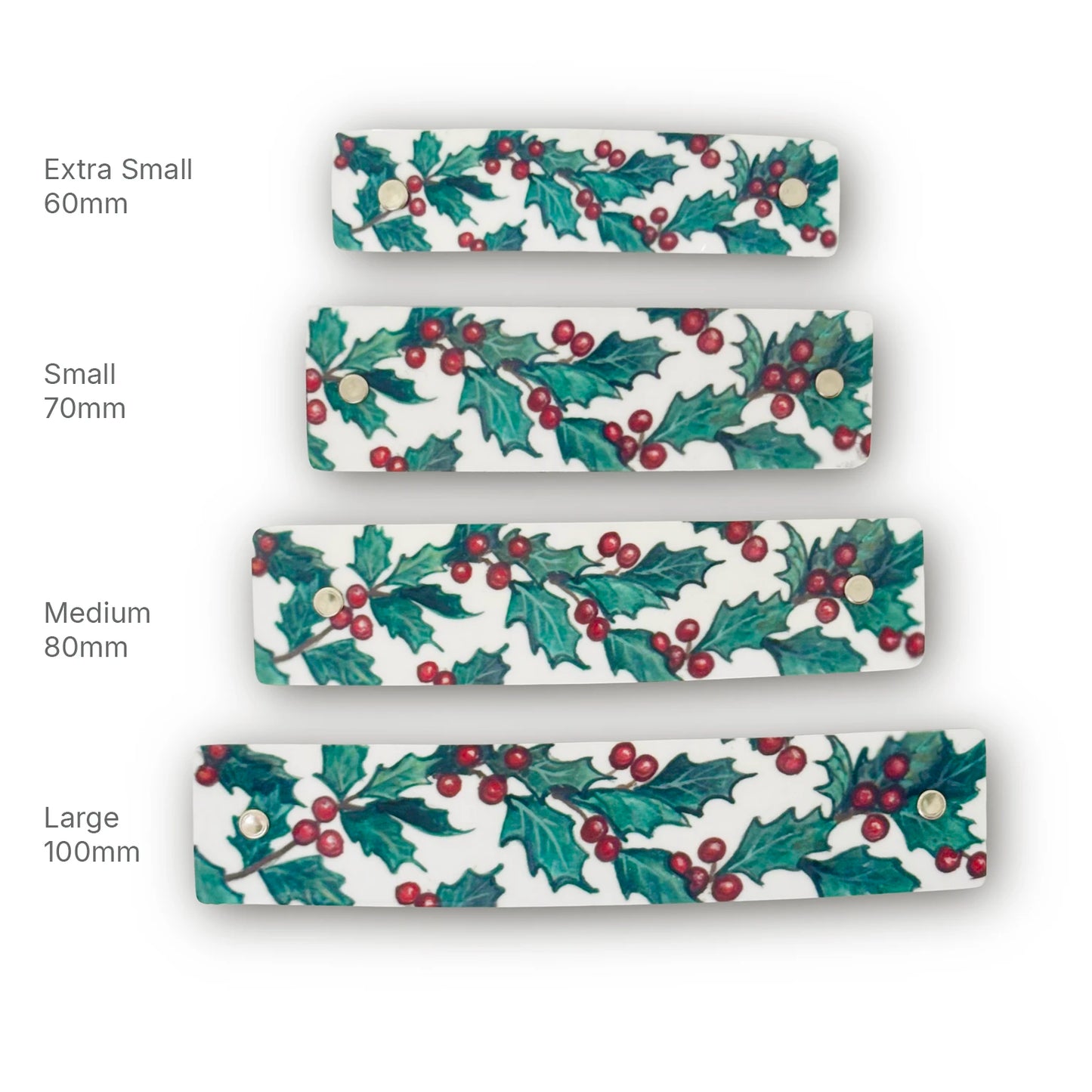 Four white French barrettes with a green holly and red berry pattern, shown in sizes Extra Small 60mm, Small 70mm, Medium 80mm, and Large 100mm.
