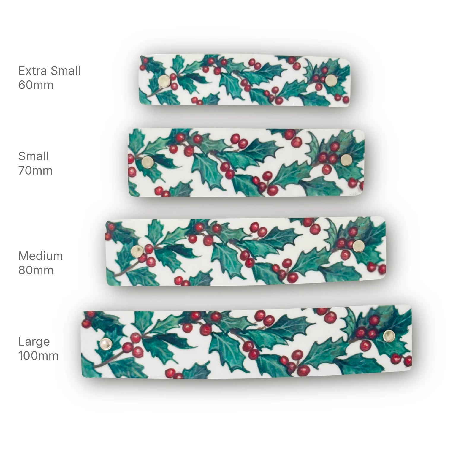 Four white French barrettes with a green holly and red berry pattern, shown in sizes Extra Small 60mm, Small 70mm, Medium 80mm, and Large 100mm.