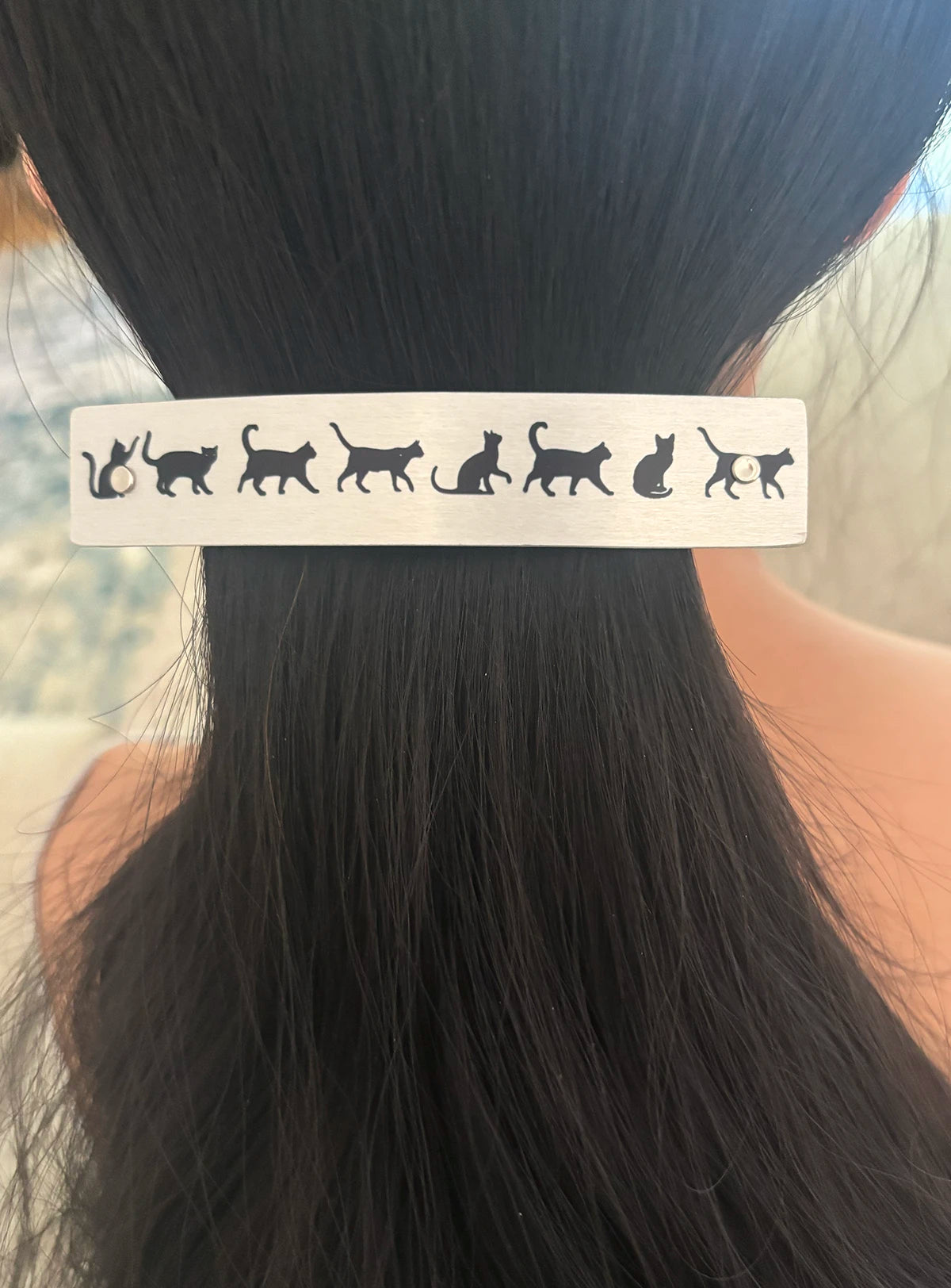 A close-up of a person's dark hair secured with a silver metal barrette,  featuring a row of black cat silhouettes.