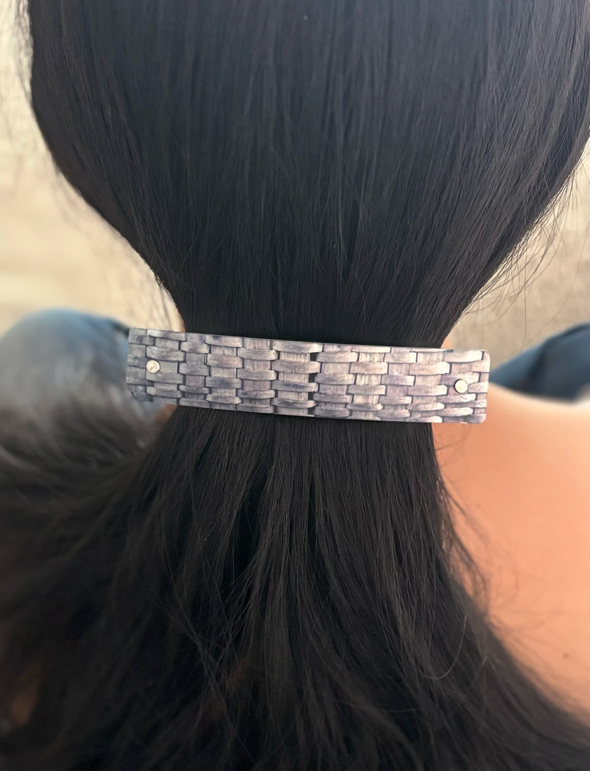 A close-up of a person's dark hair secured with a textured, woven-looking metallic hair clip or barrette.
