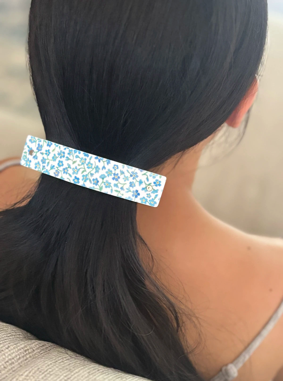 A close-up back view of a person with long black hair wearing a white hair clip decorated with a blue floral pattern.