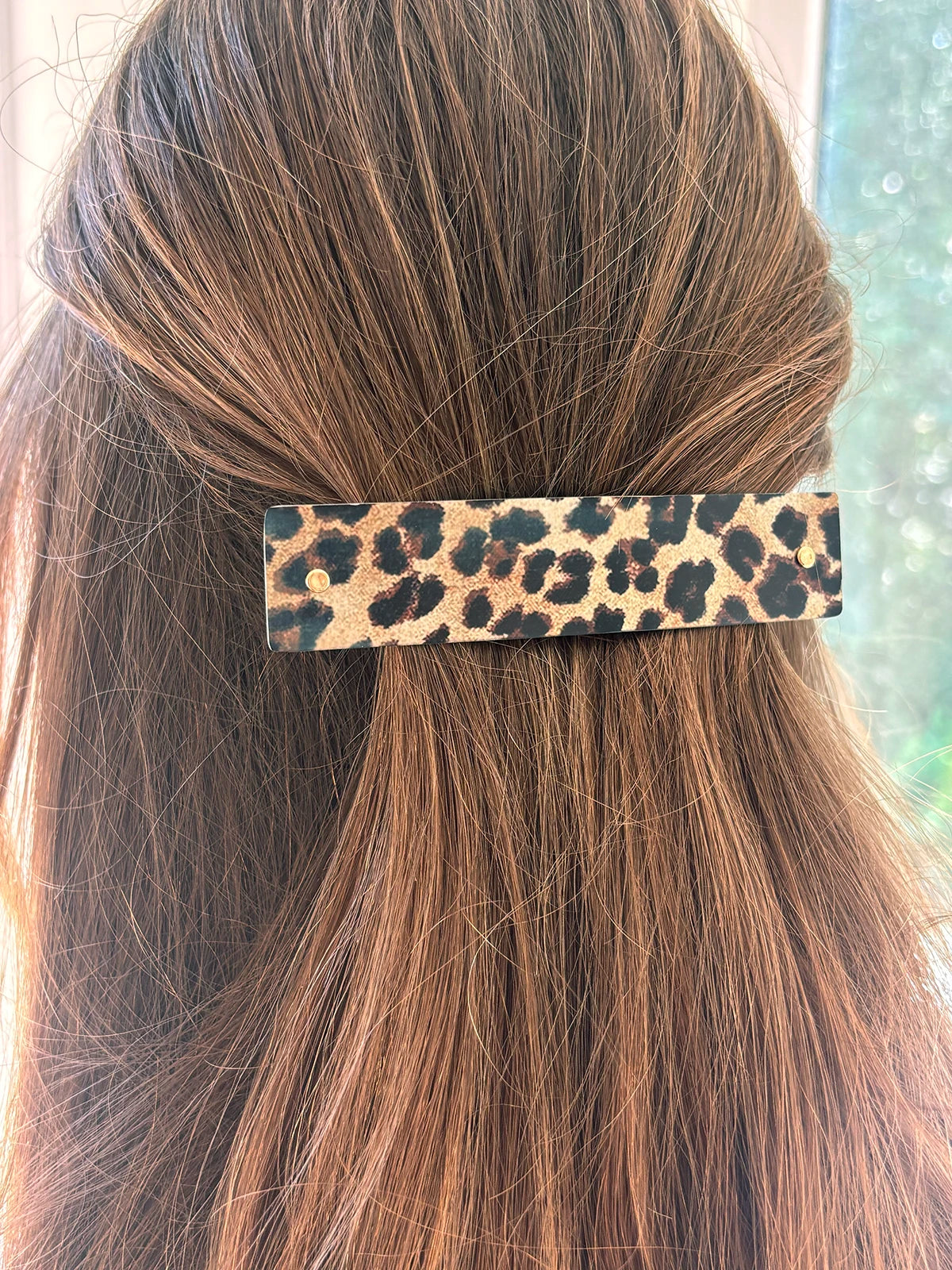 A leopard print hair clip holding a section of long, light brown hair, shown from behind.