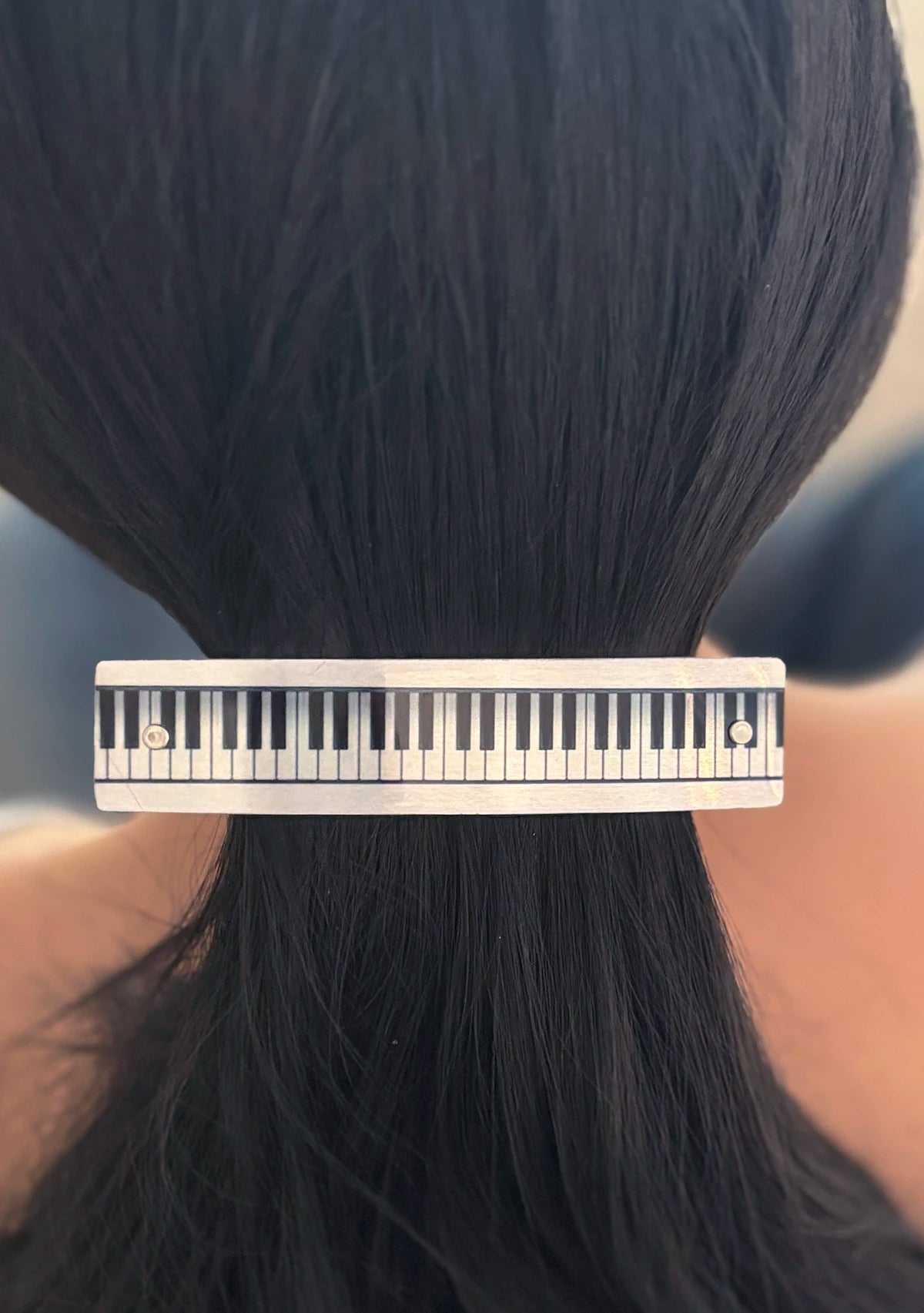 A close-up of a person's dark hair tied back with a silver-toned hair clip designed to look like a piano keyboard.