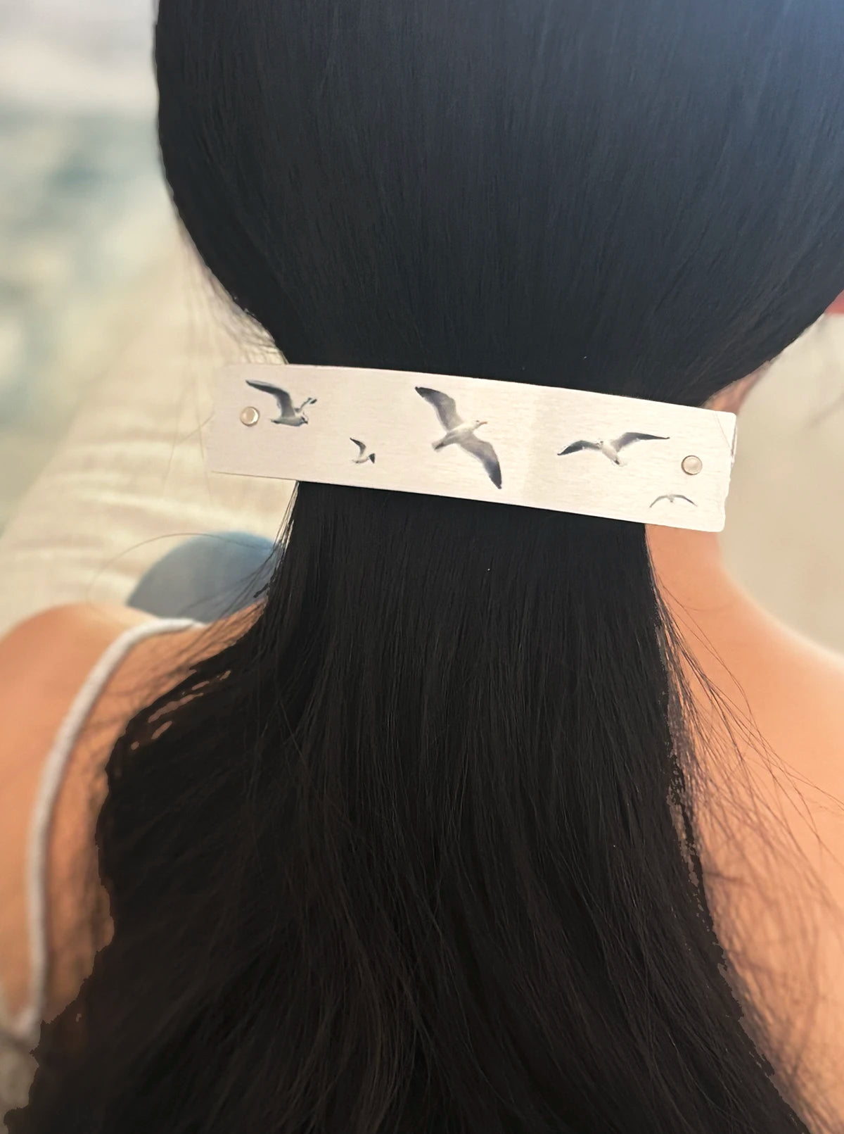A close-up of a person's dark hair secured with a silver metal hair clip decorated with flying seagull designs.