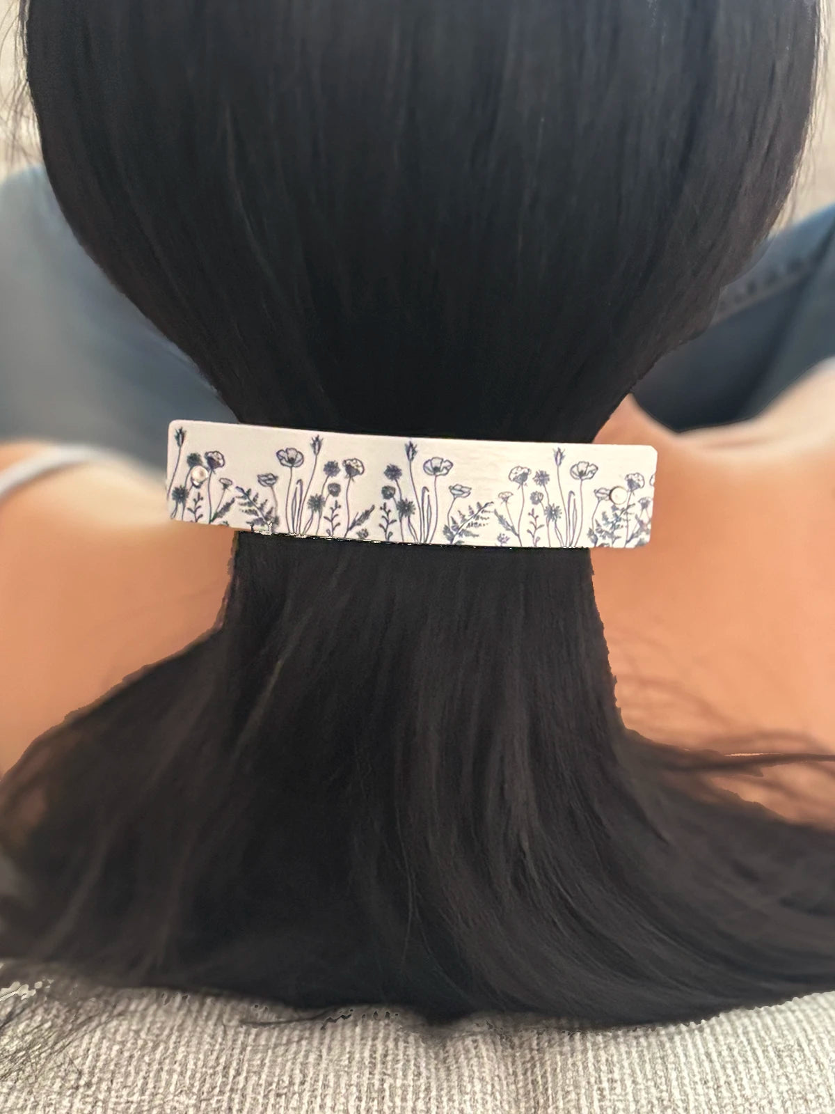 A close-up of a person's dark hair secured with a silver hair clip featuring a black ink drawn original floral and leaf pattern.