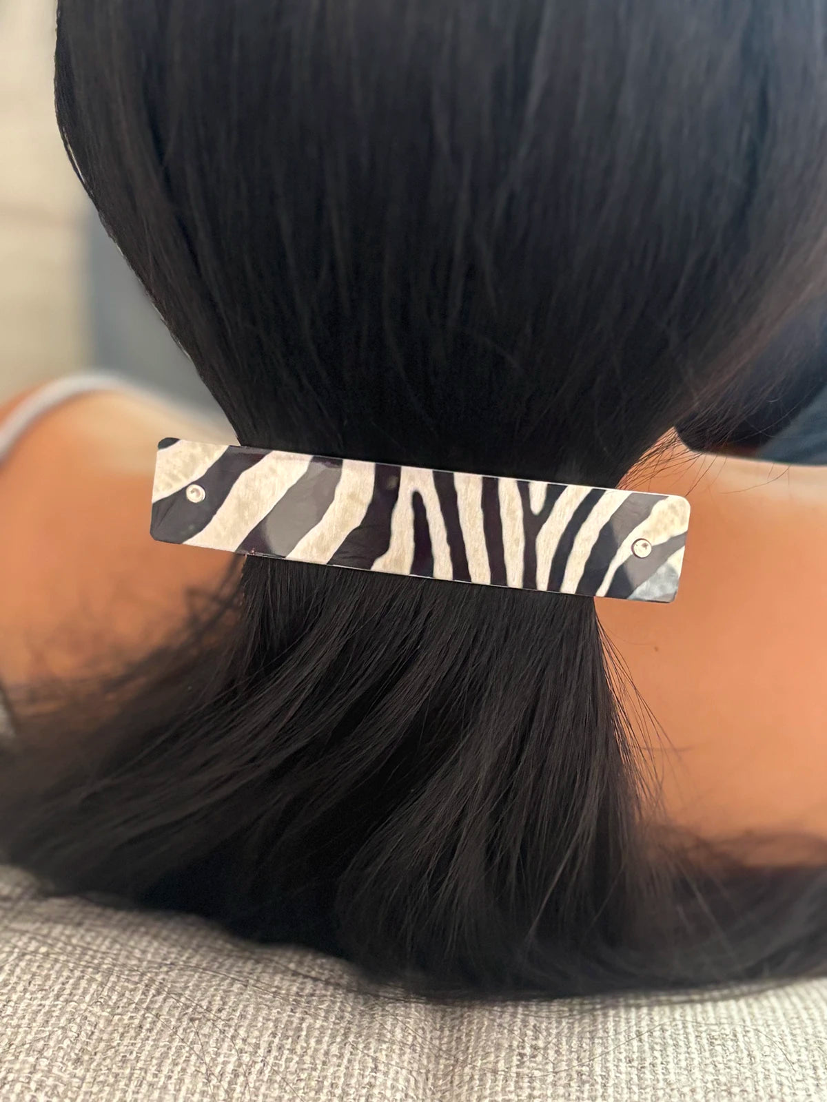 A close-up of a person's dark hair secured with a rectangular hair clip featuring a black and silver zebra print pattern.