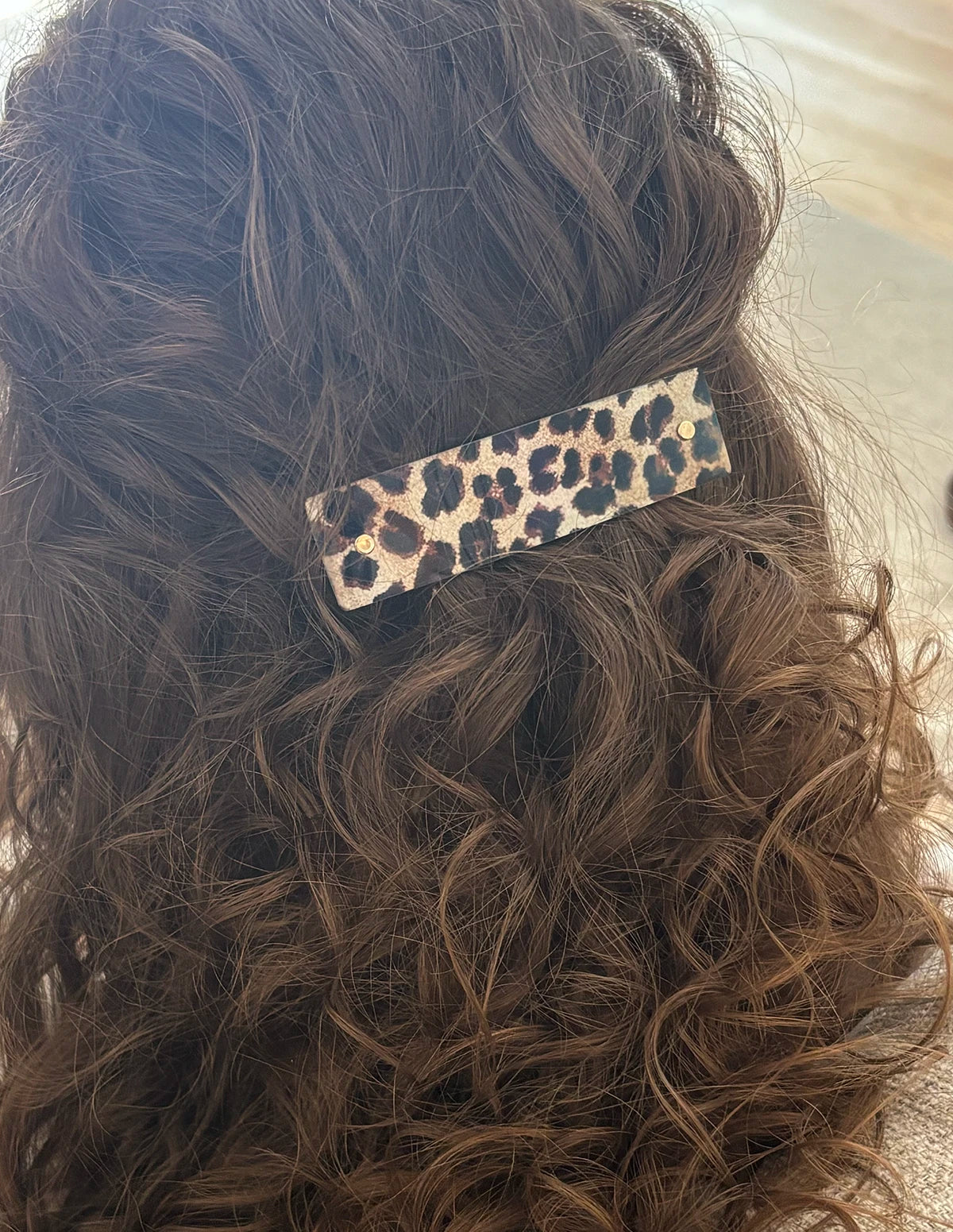 A close-up of a person's wavy brown hair secured with a leopard print hair clip.