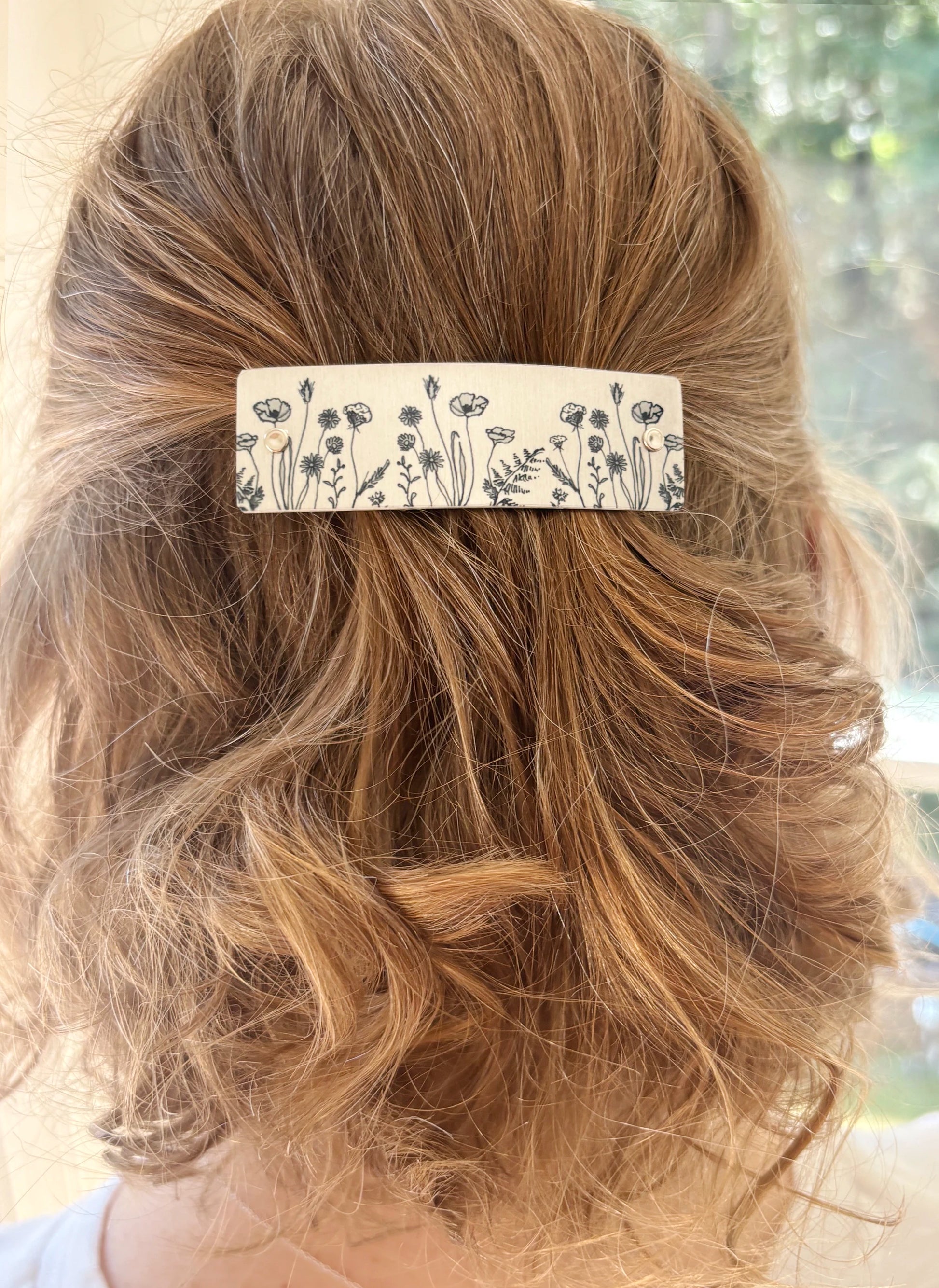 A close-up back view of a person with light brown hair wearing a rectangular hair clip adorned with a black and silver wildflower pattern.
