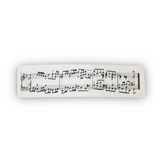 A boutique metal hair clip with printed classical music notation, shown against a plain white background.