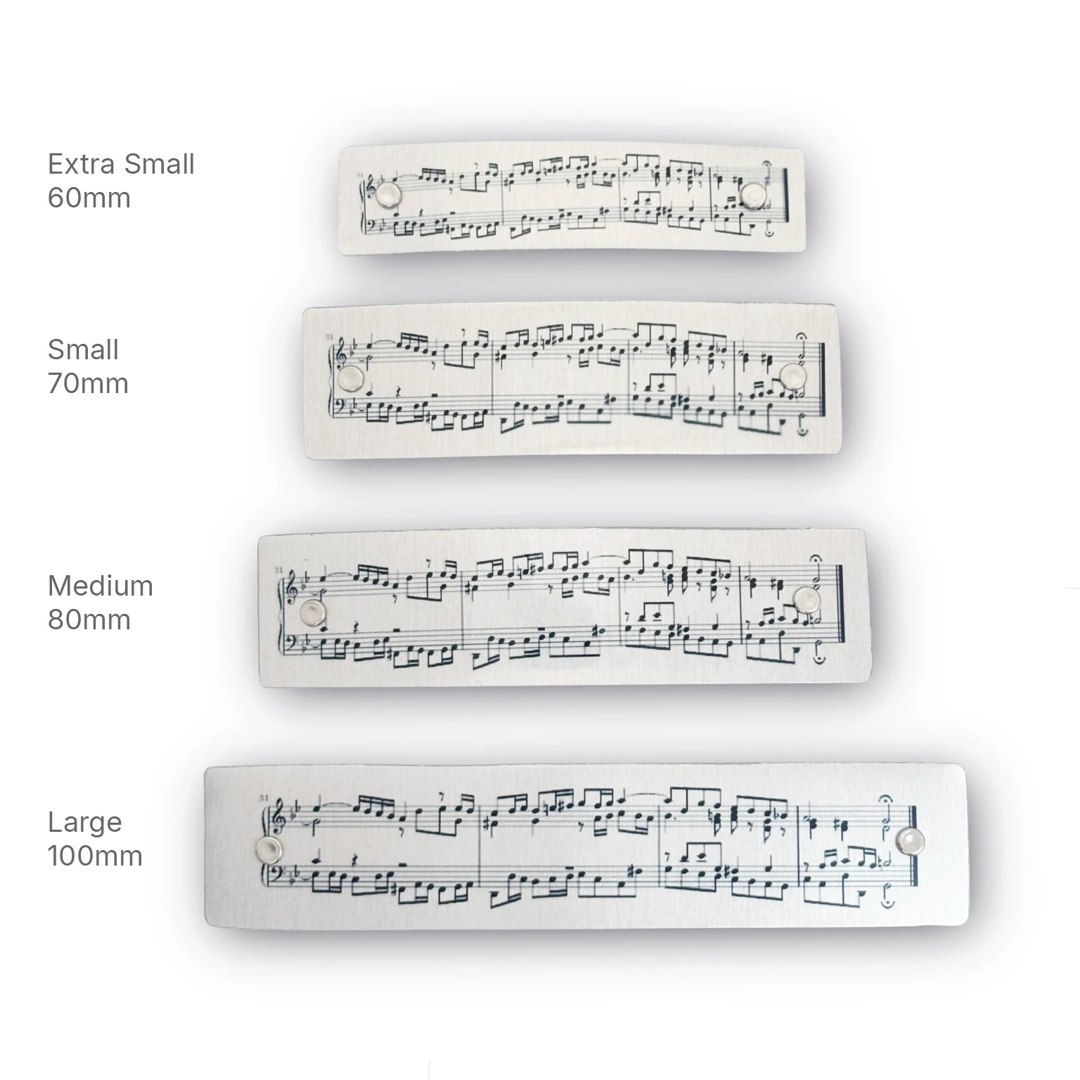 Four hair barrettes printed with sheet music, shown in four sizes labeled Extra Small 60mm, Small 70mm, Medium 80mm, and Large 100mm on a white background.