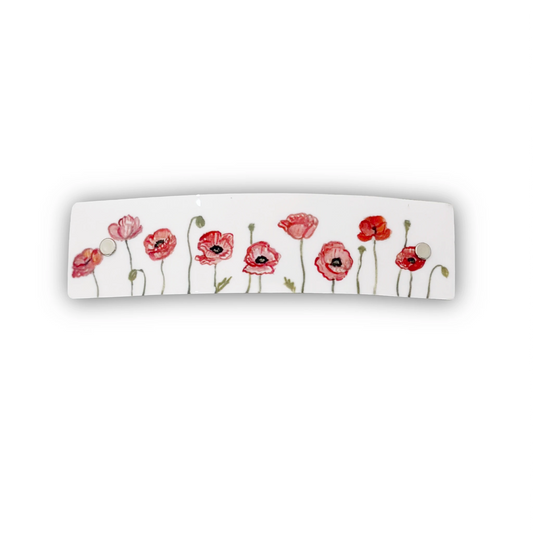 A white rectangular hair clip, decorated with a row of red and pink watercolor poppies with green stems and leaves.