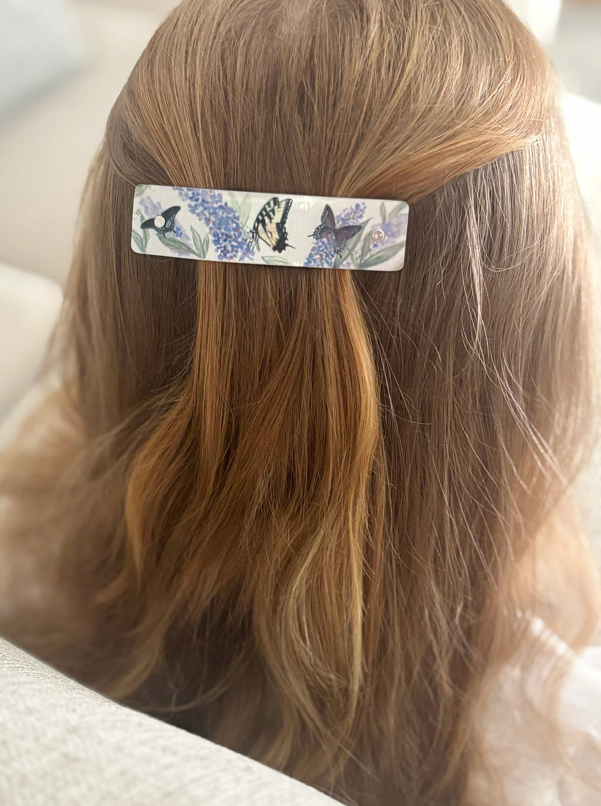 A close-up of a person's strawberry blond hair wearing a rectangular hair clip decorated with a butterfly and floral pattern.