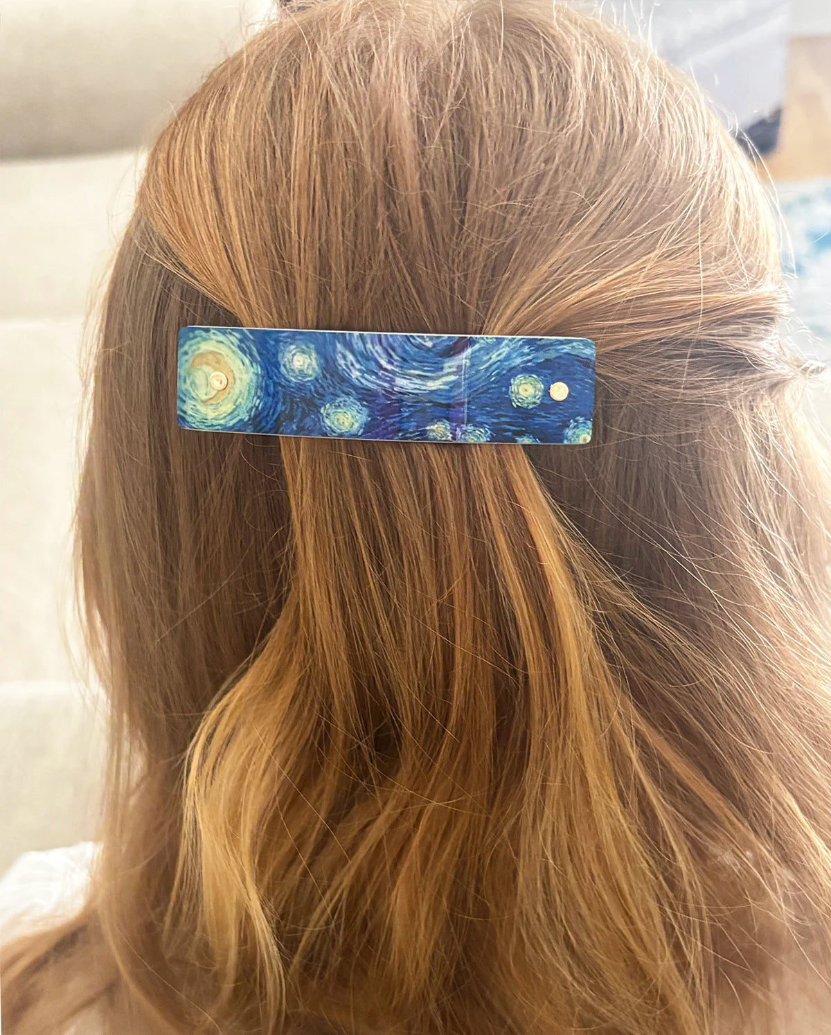 A close-up of a person's light brown hair wearing a rectangular hair clip decorated with a blue and yellow Starry Night painting pattern.