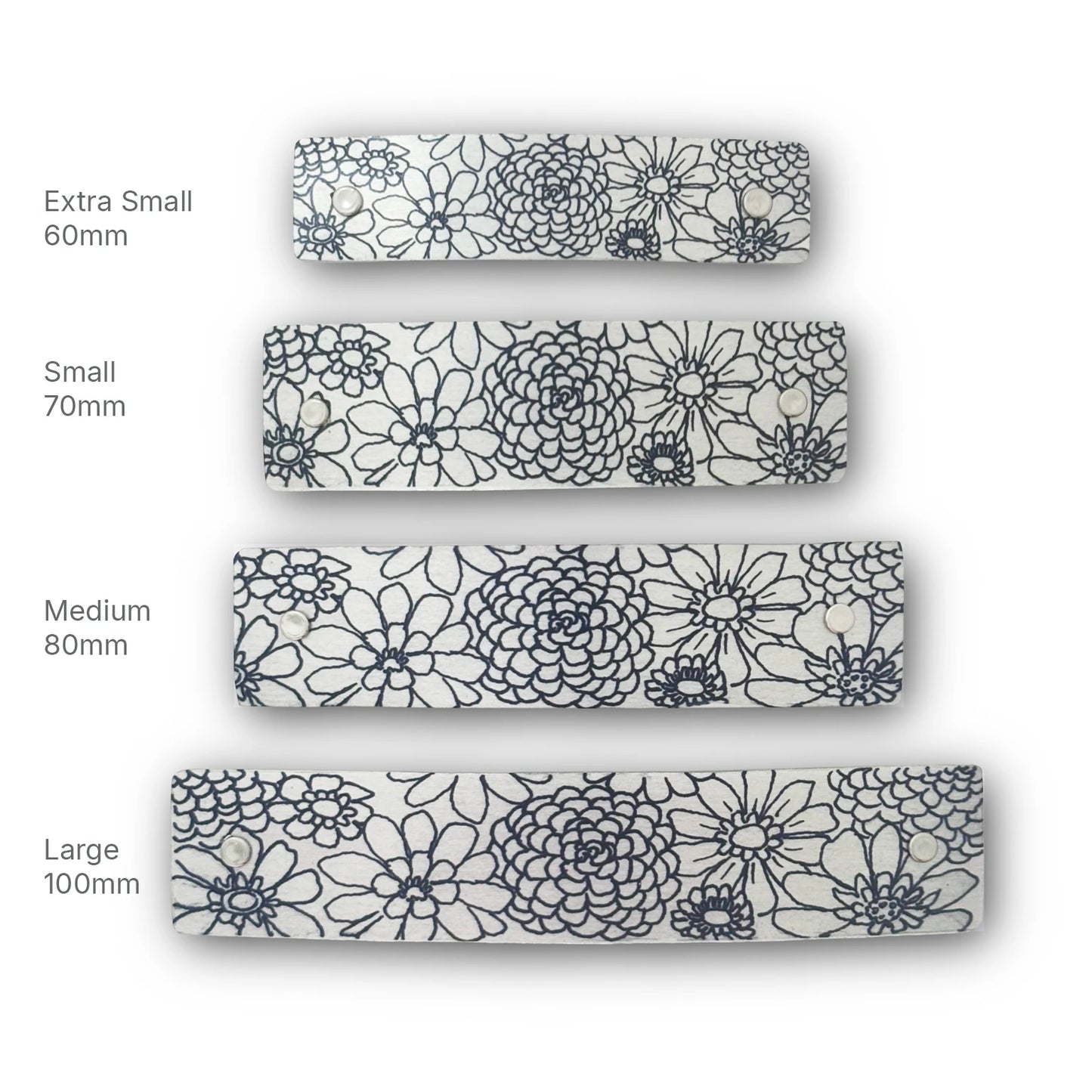 Four French barrettes shown in different sizes labeled Extra Small 60mm, Small 70mm, Medium 80mm, and Large 100mm, all featuring a black zinnia floral line-art pattern on a silver background.