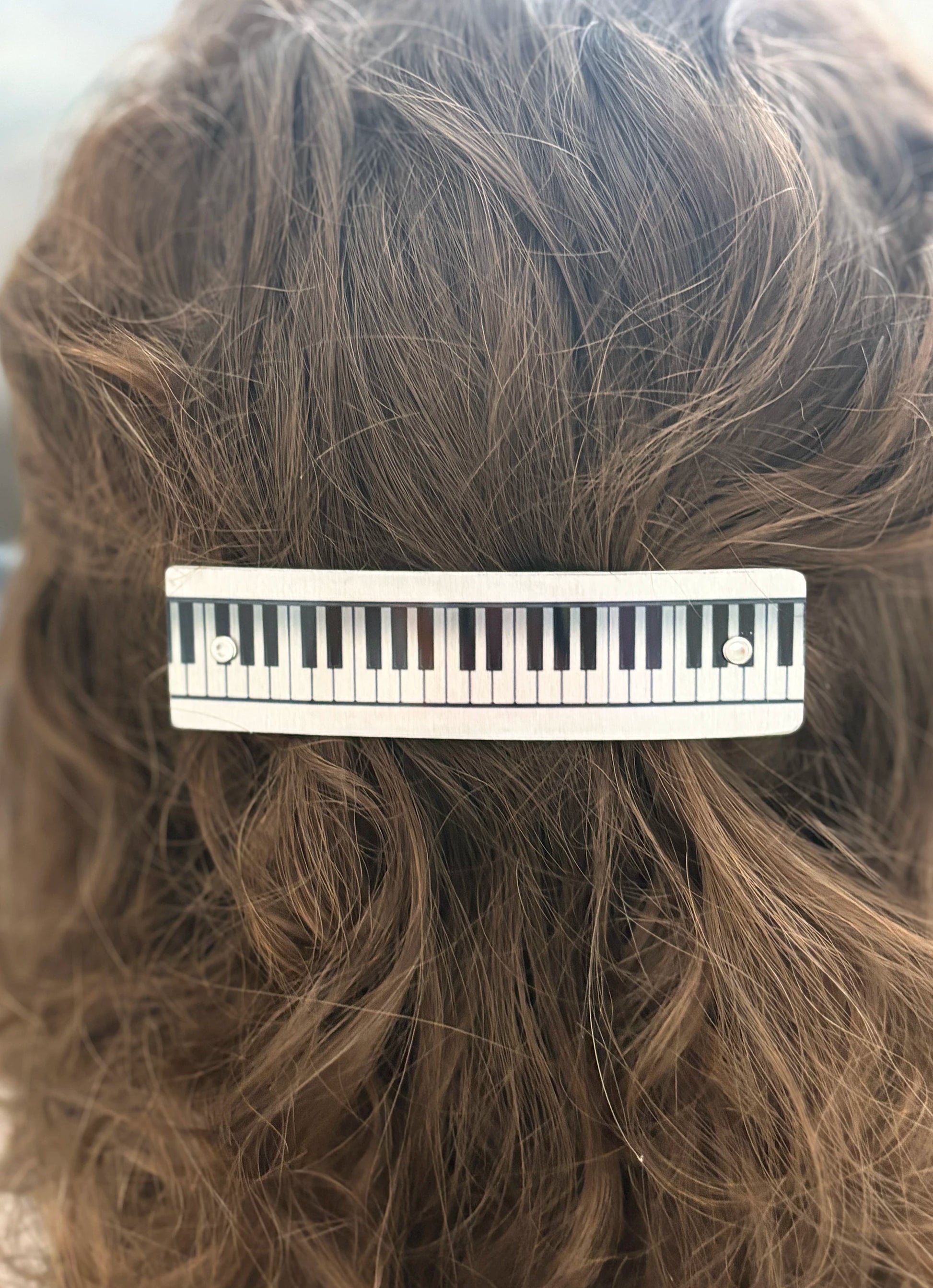 A close-up of brown hair secured with a silver-toned hair clip designed to look like a piano keyboard.