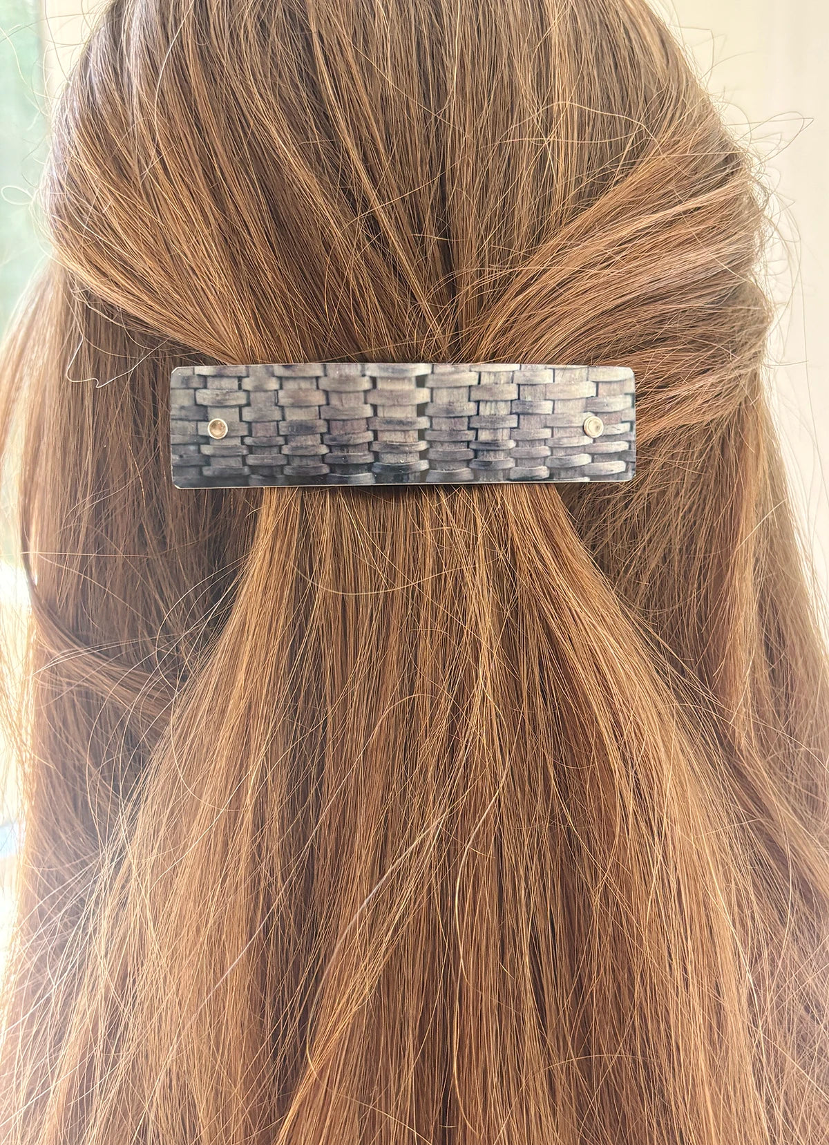 A close-up of a person's light brown hair secured with a textured, rectangular hair clip in a woven pattern.