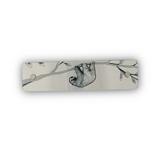 Original art of a sloth hand=ging from a branch, featured on a silver tone metal boutique hair clip for women.