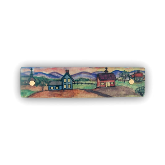 A rectangular hair clip featuring a hand-painted folk art landscape with houses, mountains, and trees, shown against a plain white background.