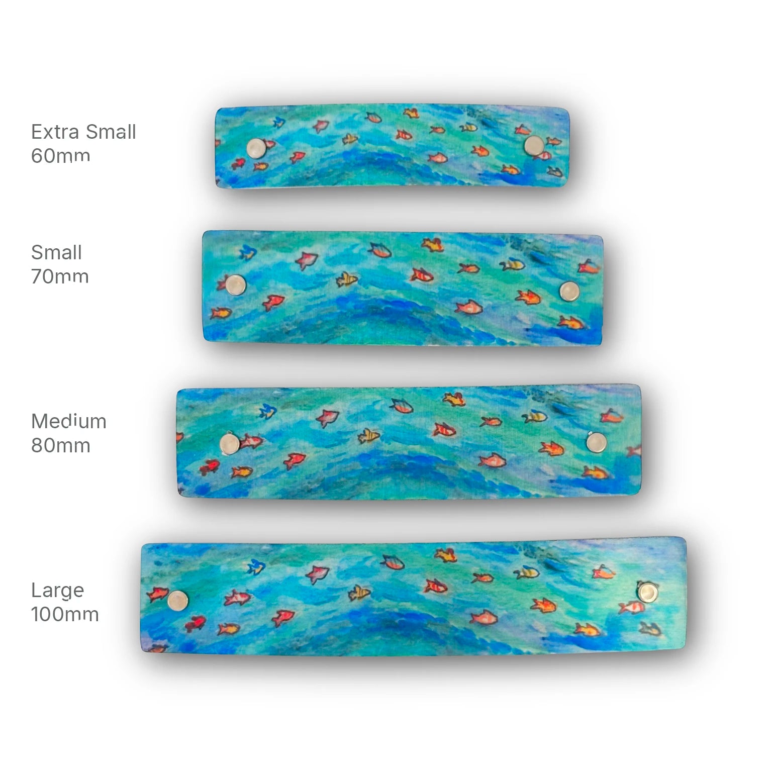 Four rectangul boutique hair barrettes in different sizes (Extra Small 60mm, Small 70mm, Medium 80mm, Large 100mm) featuring a blue and green watercolor-style fish pattern with small silver rivets, shown on a white background with size labels.