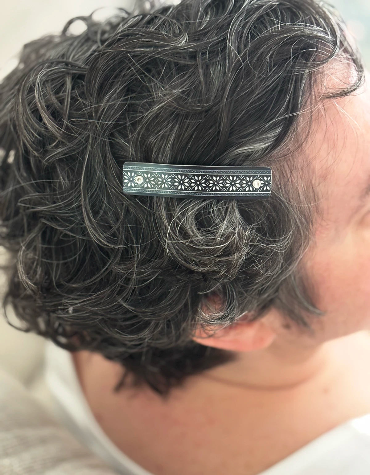 A close-up of a person's dark curly hair with a black and silver-toned barrette hair clip featuring an intricate Nordic star pattern.