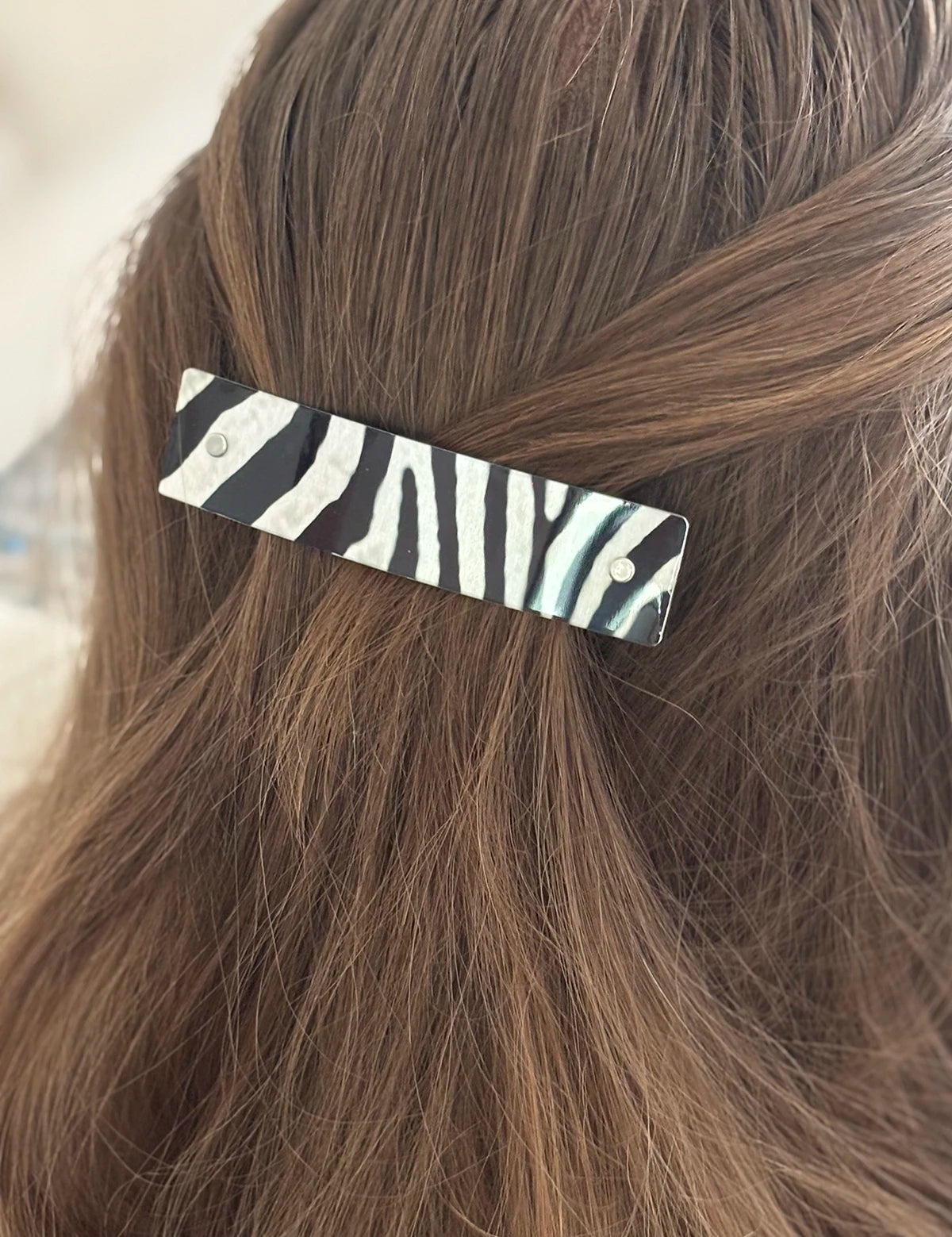 A close-up of brown hair secured with a rectangular hair clip featuring a black and white zebra print pattern.